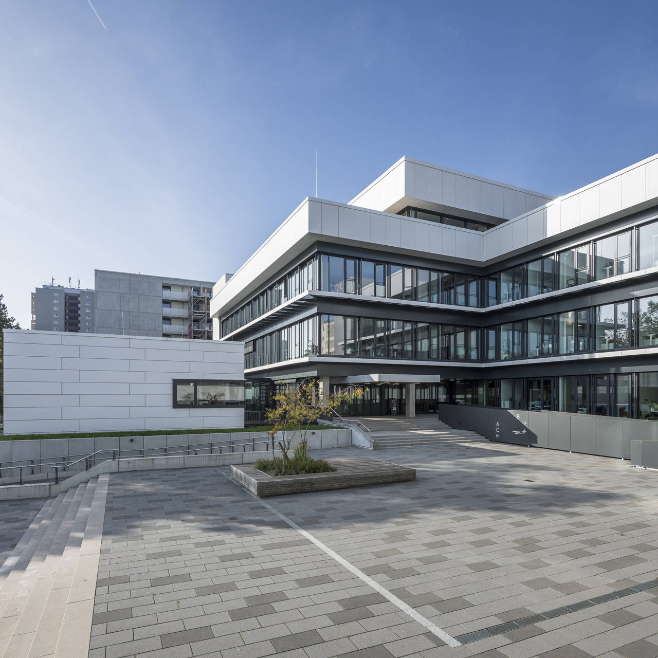 Modern university building with a large terrace and blue sky in the background.