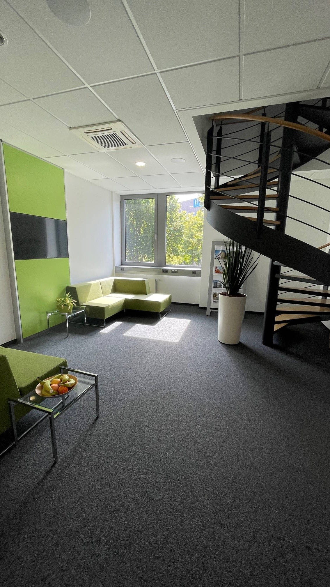 Modernes Büro mit grüner Sitzecke, Wendeltreppe und Fenster mit Blick ins Grüne.
