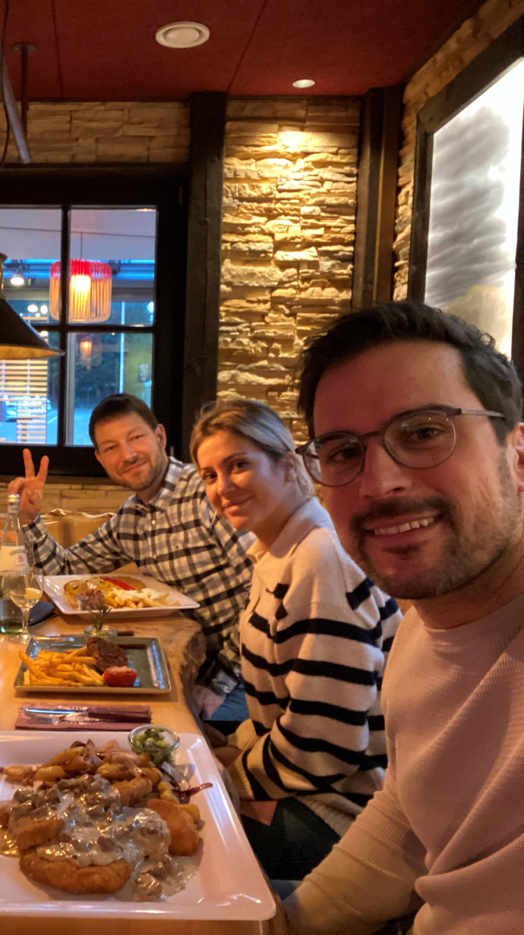 Eine Gruppe von fünf Personen befindet sich gemeinsam in einem Restaurant, vor ihnen stehen Teller mit verschiedenen Gerichten und Getränken.