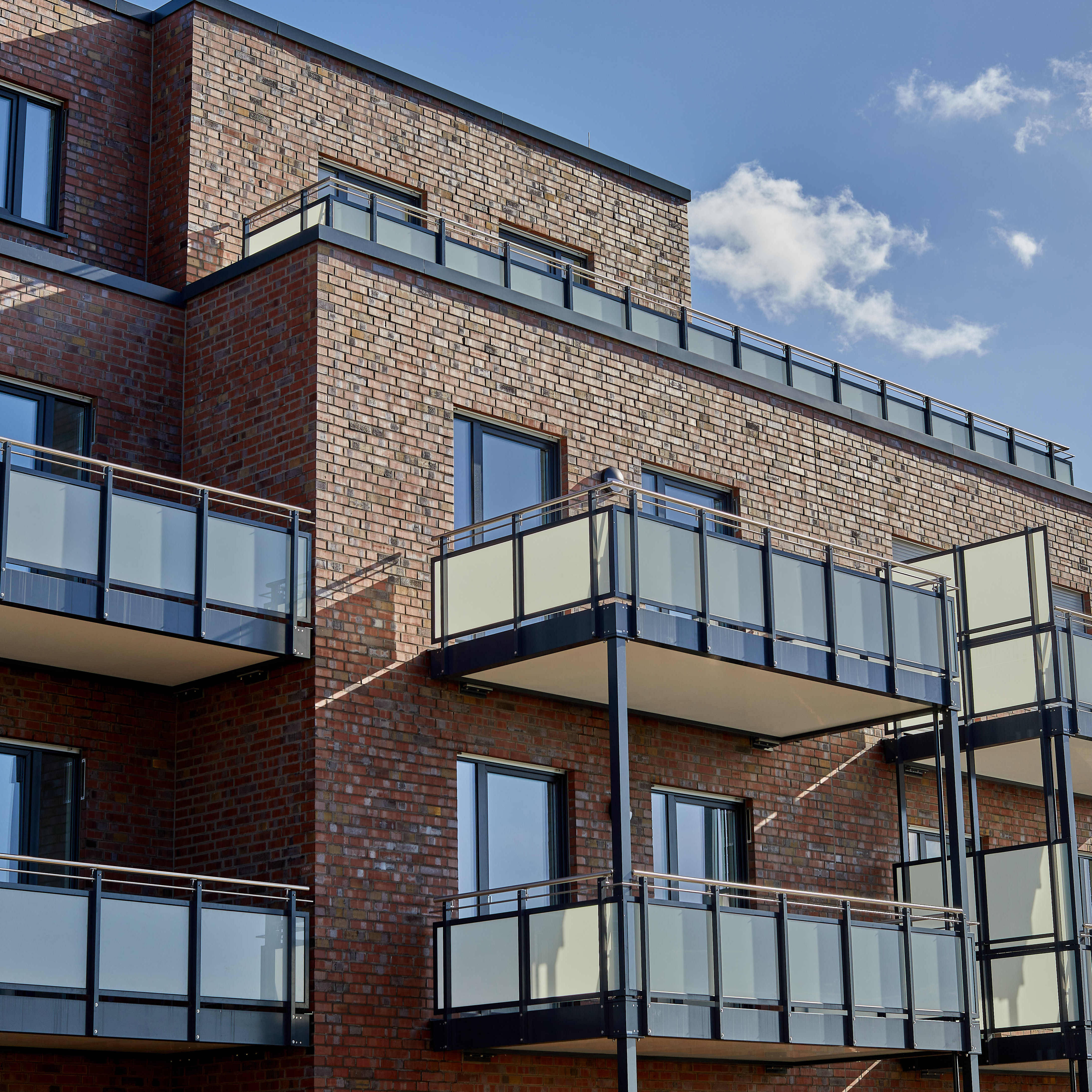 Apartment building with modern brick façade and balconies under a blue sky.