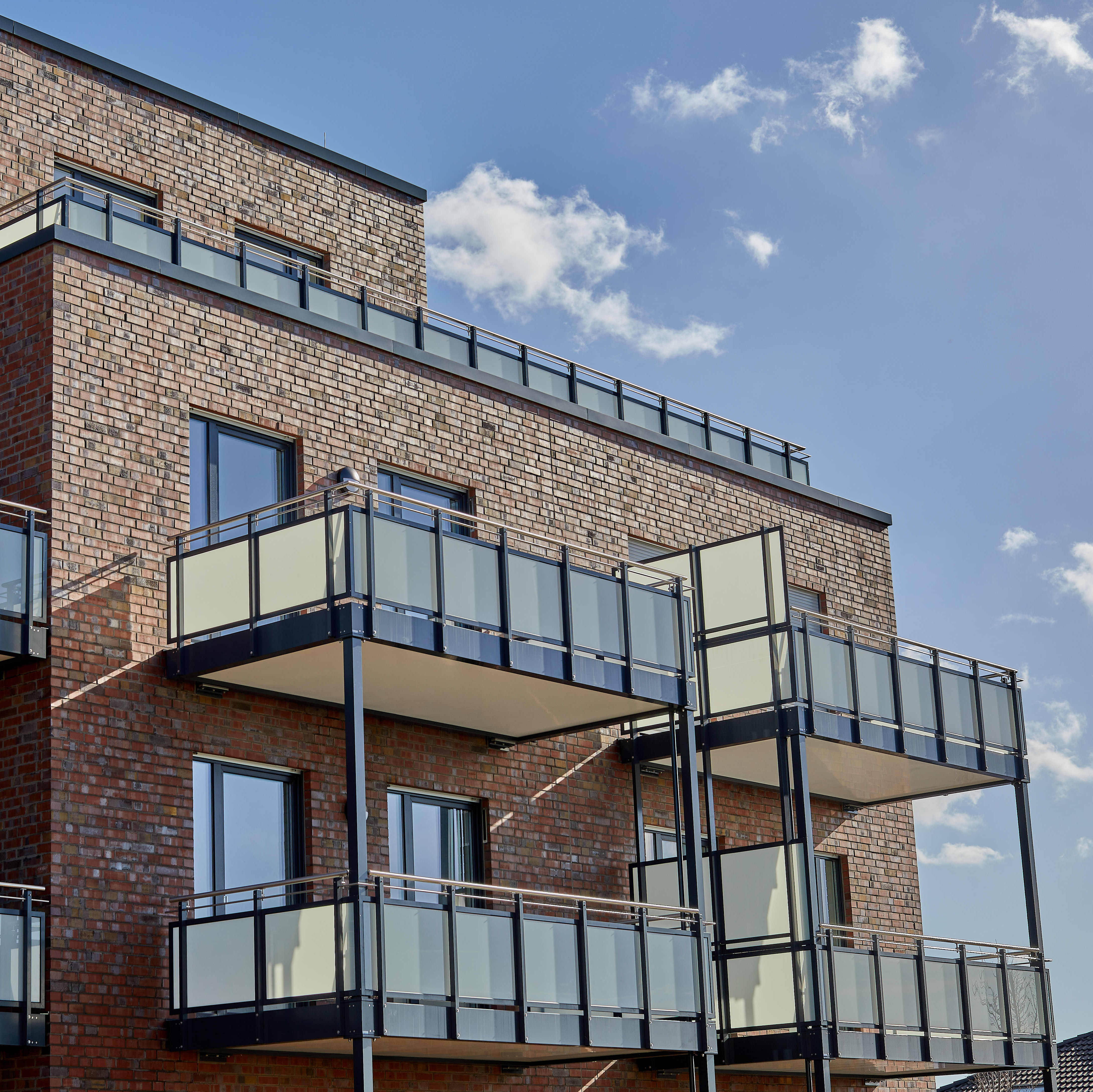 Multi-storey residential building with brick façade and glass balconies, under a blue sky.