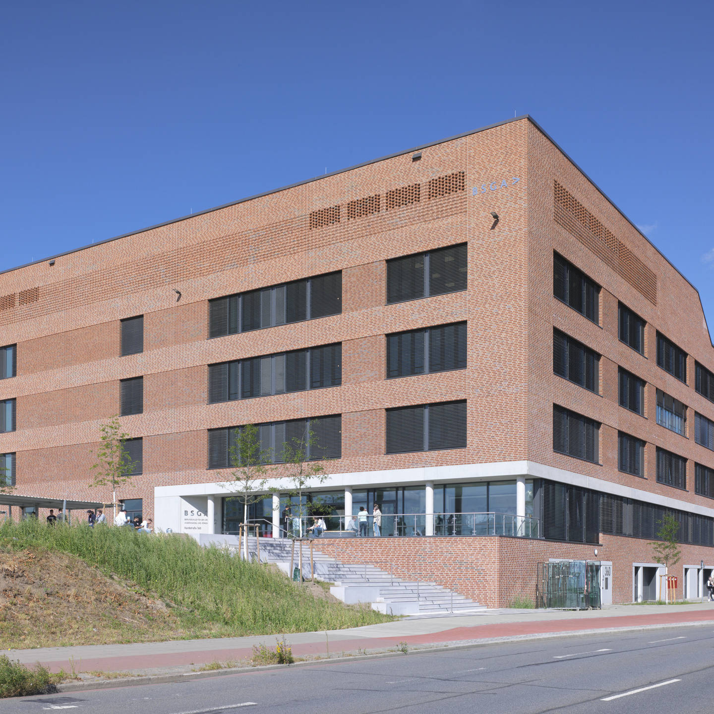 Rotes Backsteingebäude mit großen Fenstern, moderne Architektur, blauer Himmel im Hintergrund.