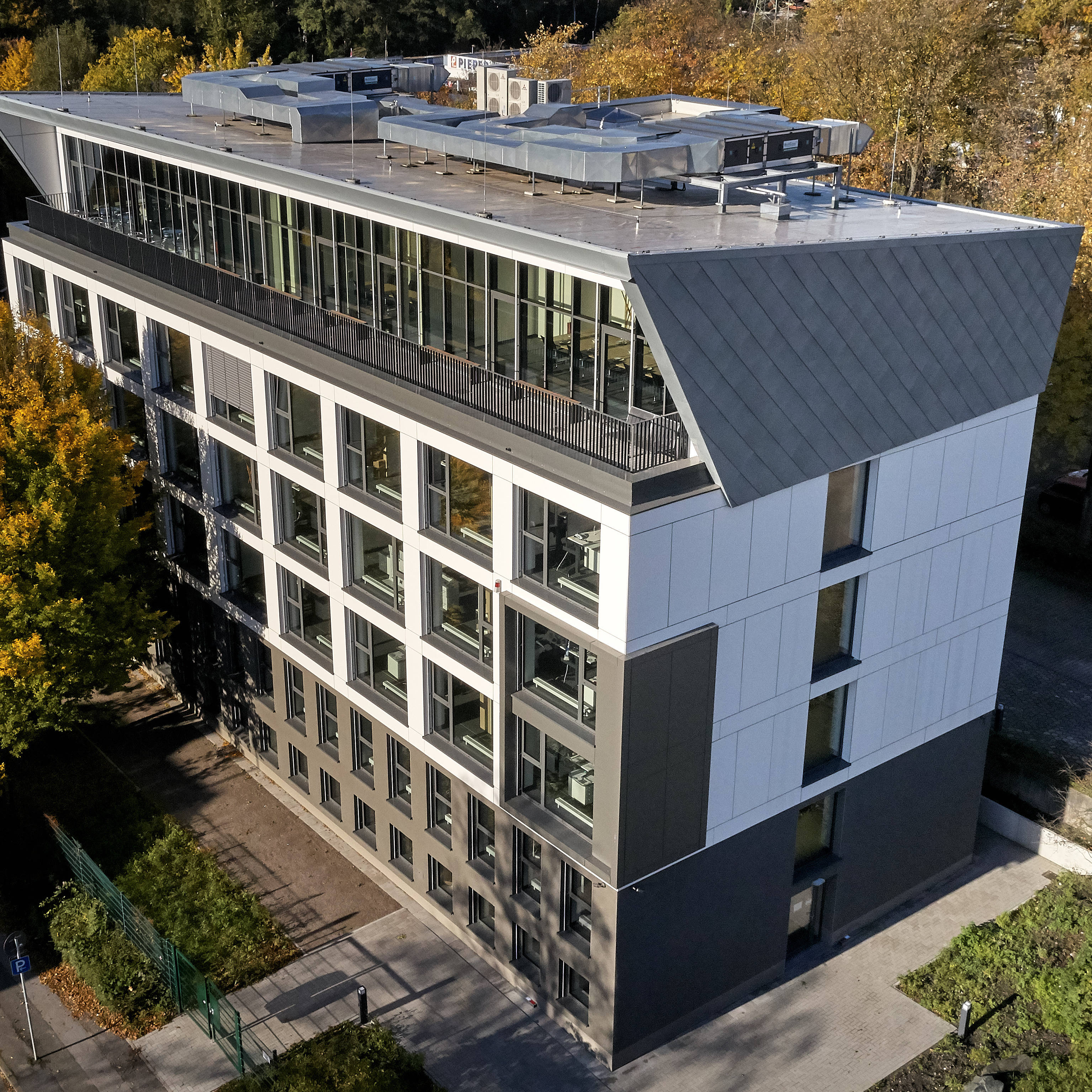 Modernes Bürogebäude mit großen Fenstern, umgeben von herbstlichen Bäumen und Straßenansicht von oben.