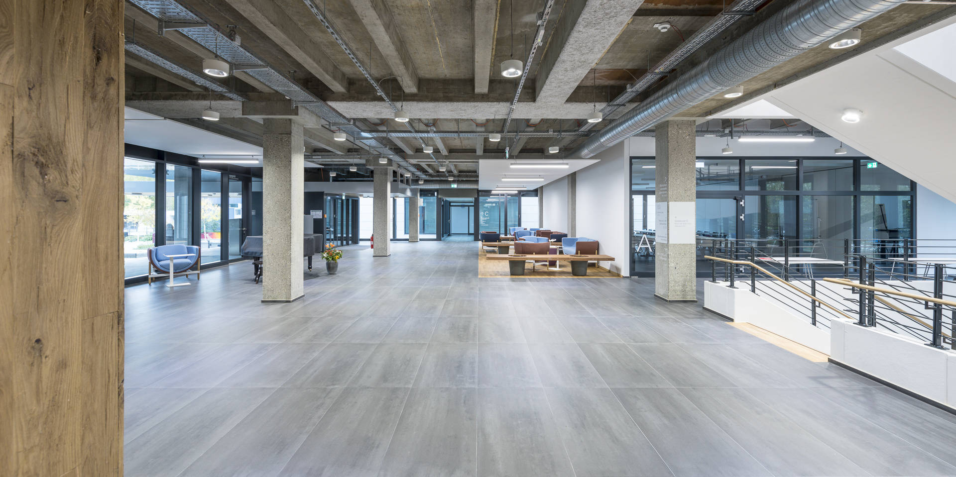 Moderner, offener Büroraum mit Betonwänden, Glastrennwänden und Sitzbereichen im Industrie-Design.