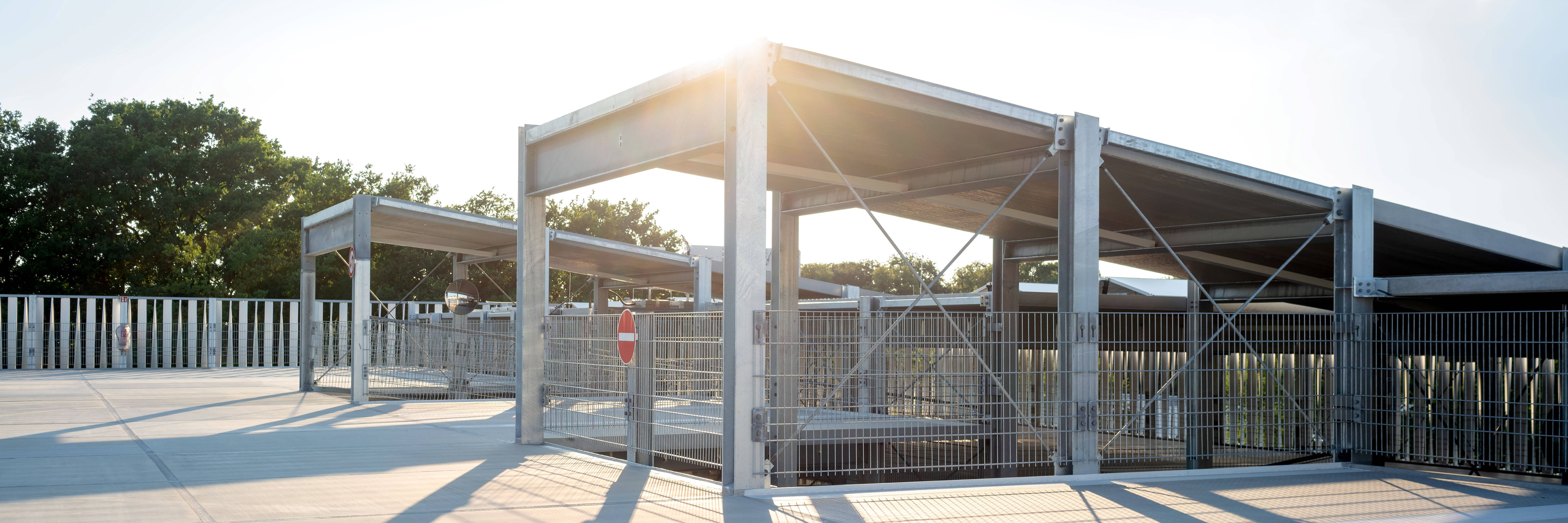 Offenes Parkhaus bei Sonnenuntergang mit Metallgerüsten und Schatten auf dem Betonboden.