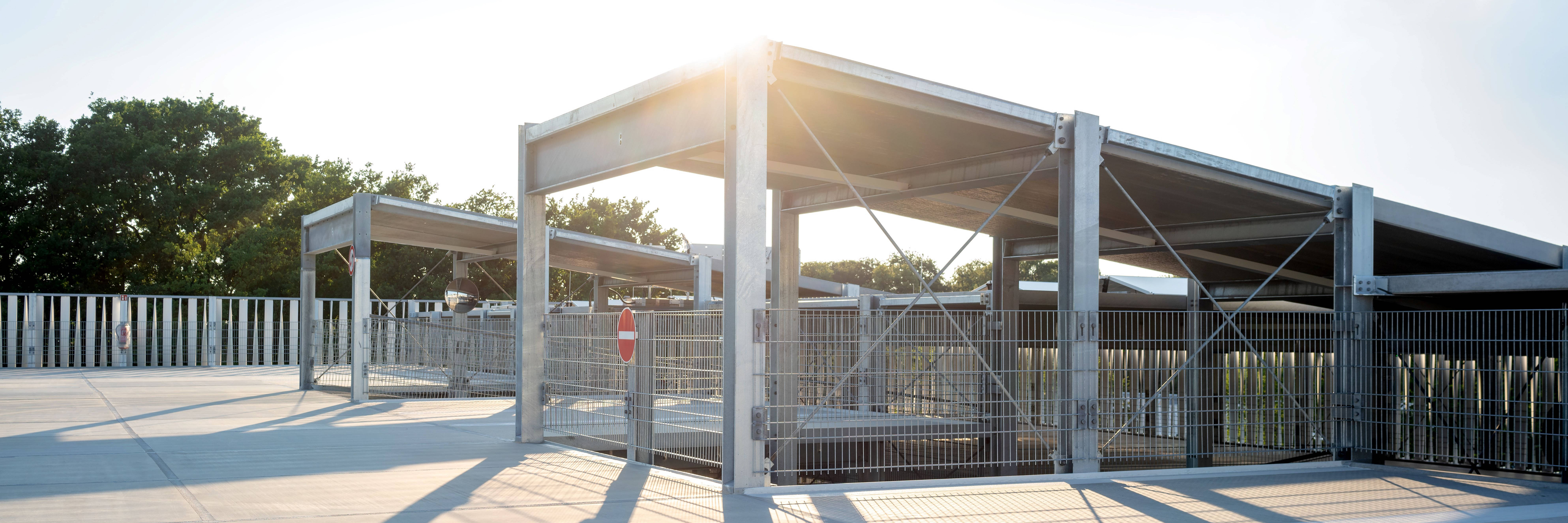 Offenes Parkhaus bei Sonnenuntergang mit Metallgerüsten und Schatten auf dem Betonboden.