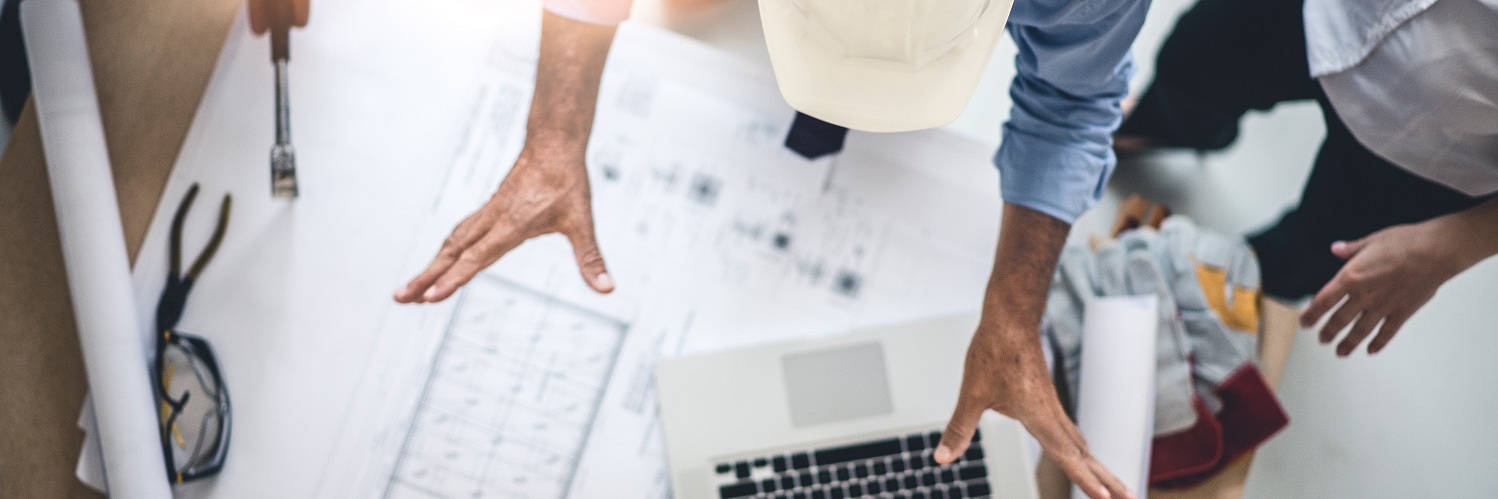 Architektenteam diskutiert Baupläne an einem Tisch mit Laptop und Werkzeugen.