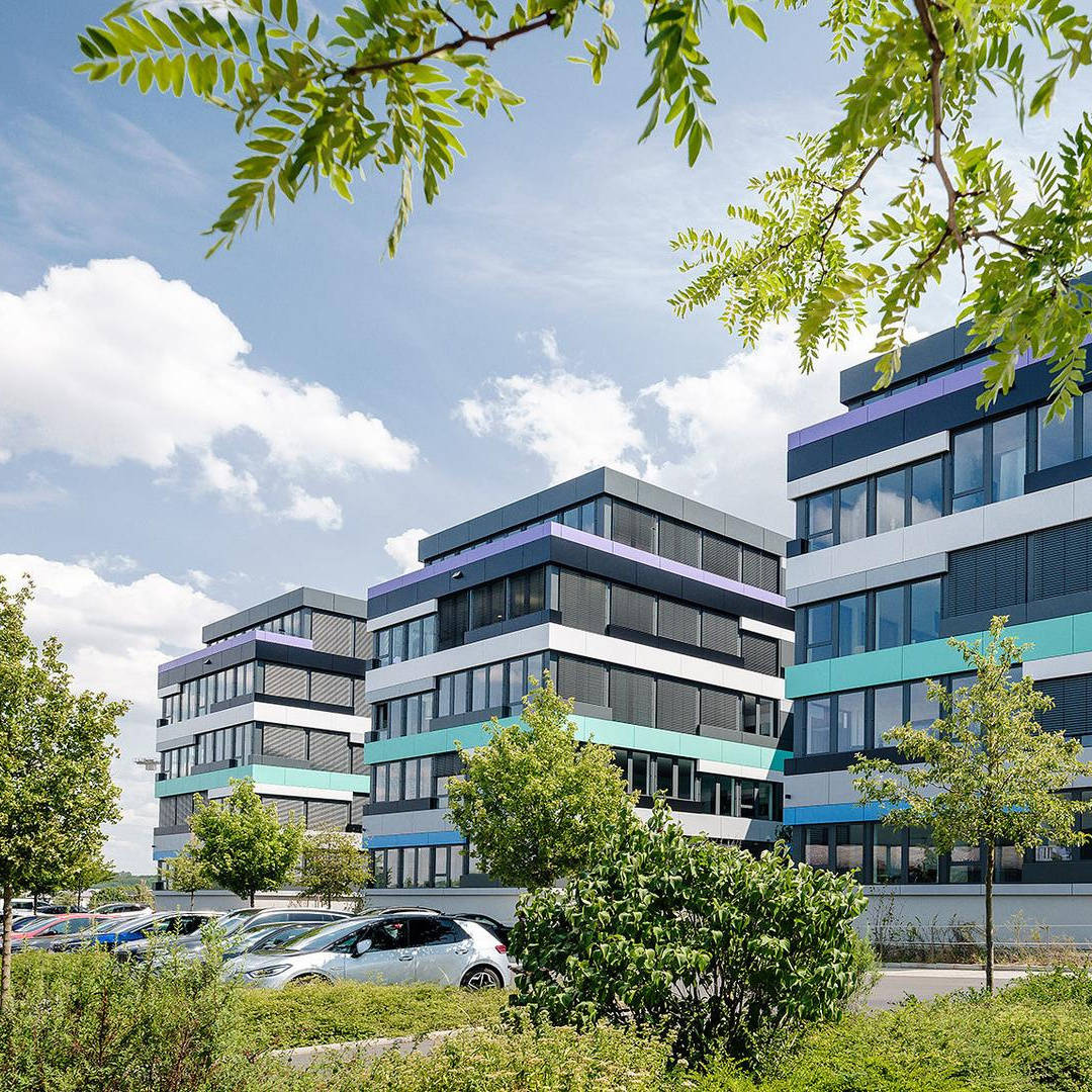 Three buildings with a colourful facade and a car park and trees in the foreground.
