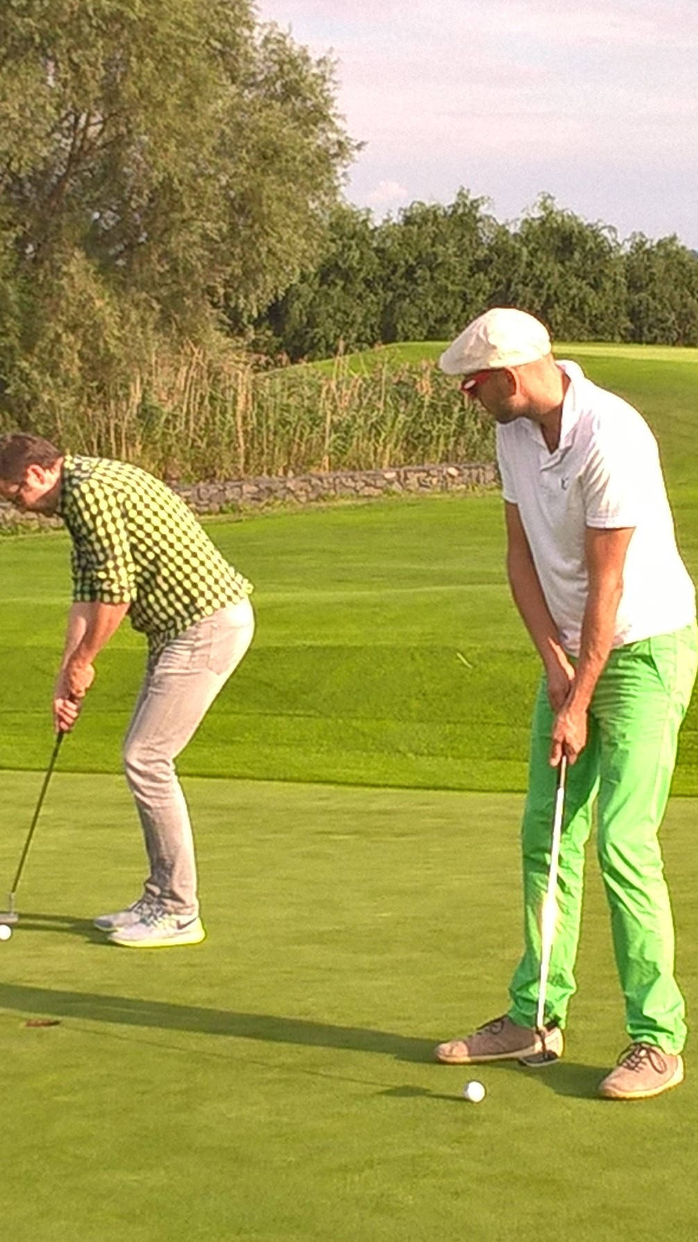 Zwei Männer beim Golfspielen auf einem grünen Fairway, konzentrieren sich auf ihren nächsten Putt.