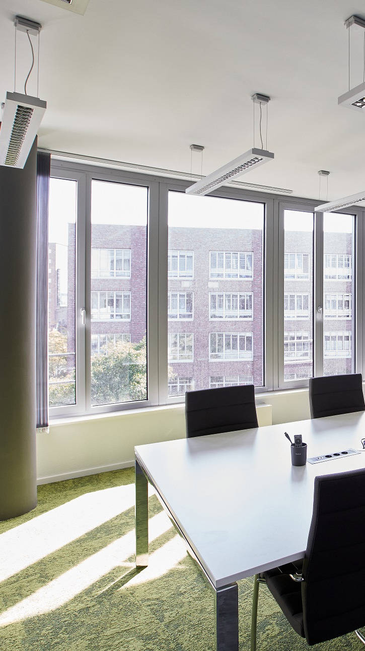 Moderner Konferenzraum mit großem Tisch, schwarzen Stühlen und Moos-Wanddekoration, blickt auf Bürogebäude.