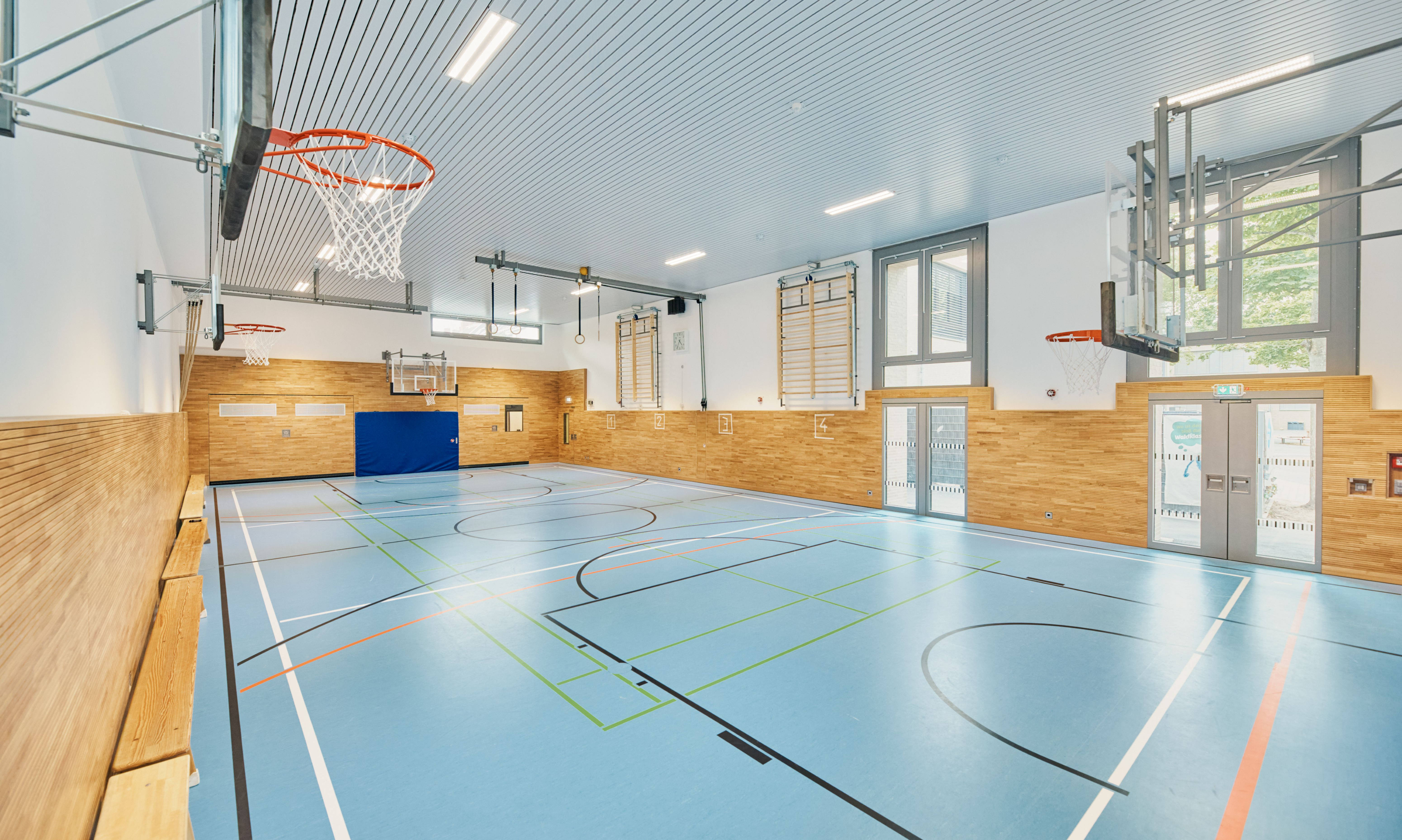 A modern, bright sports hall with basketball hoops and blue lines on the floor.