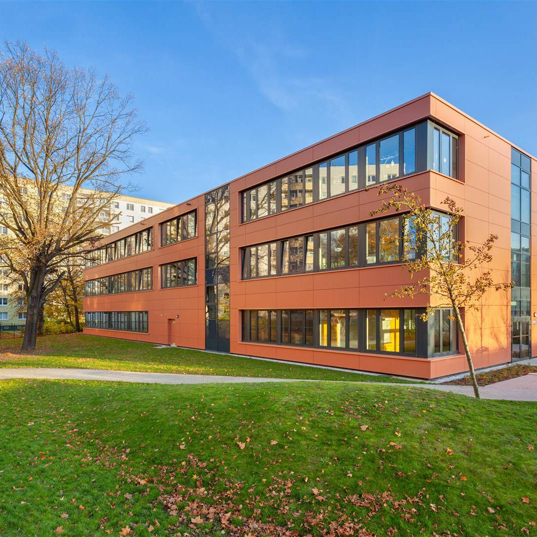 Moderner, orangefarbener Bürokomplex im Herbst, umgeben von Wohnhochhäusern und Bäumen auf grünem Rasen.