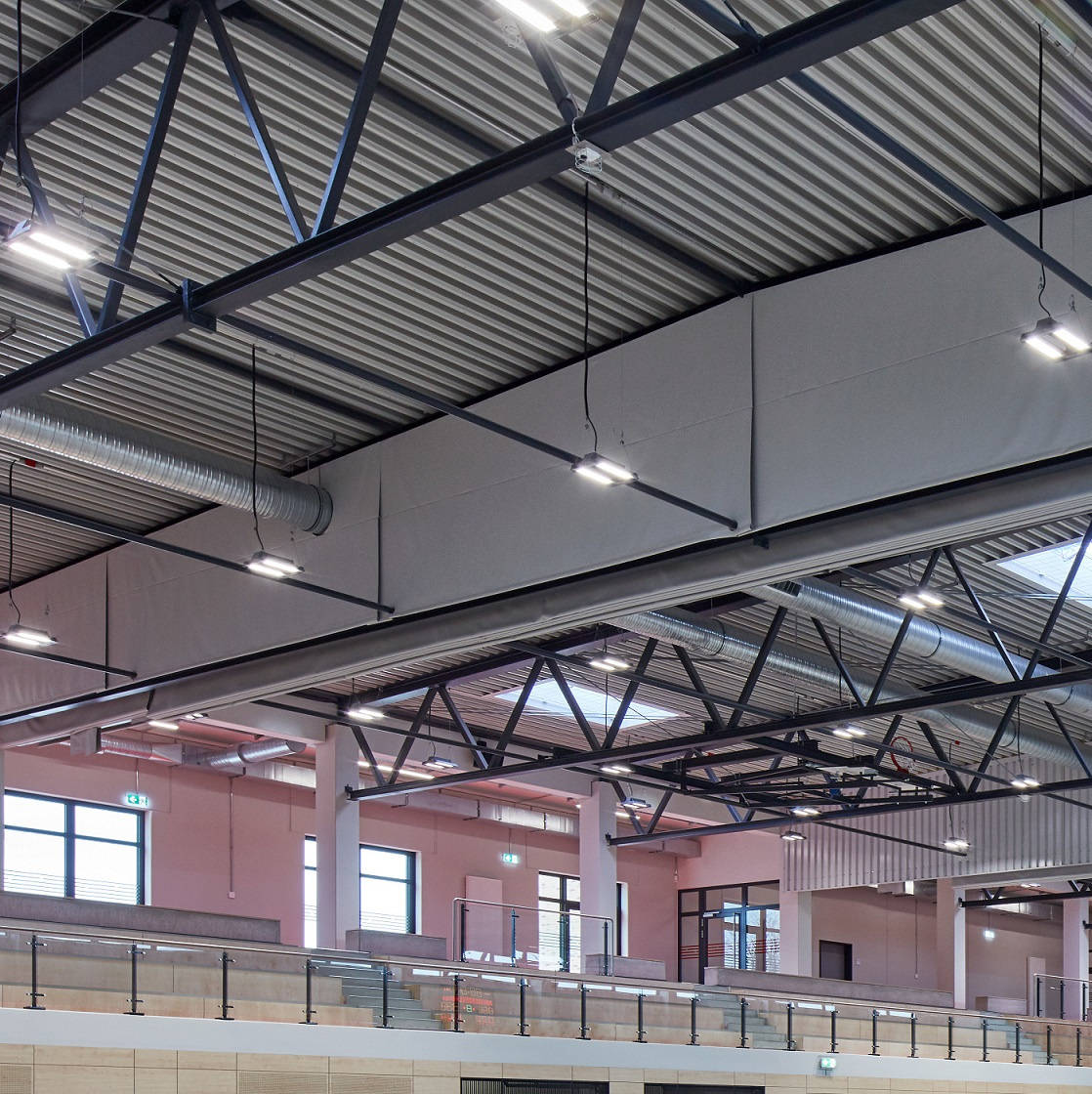 Ceiling view of a modern sports hall with visible ventilation elements and a basketball hoop holder.