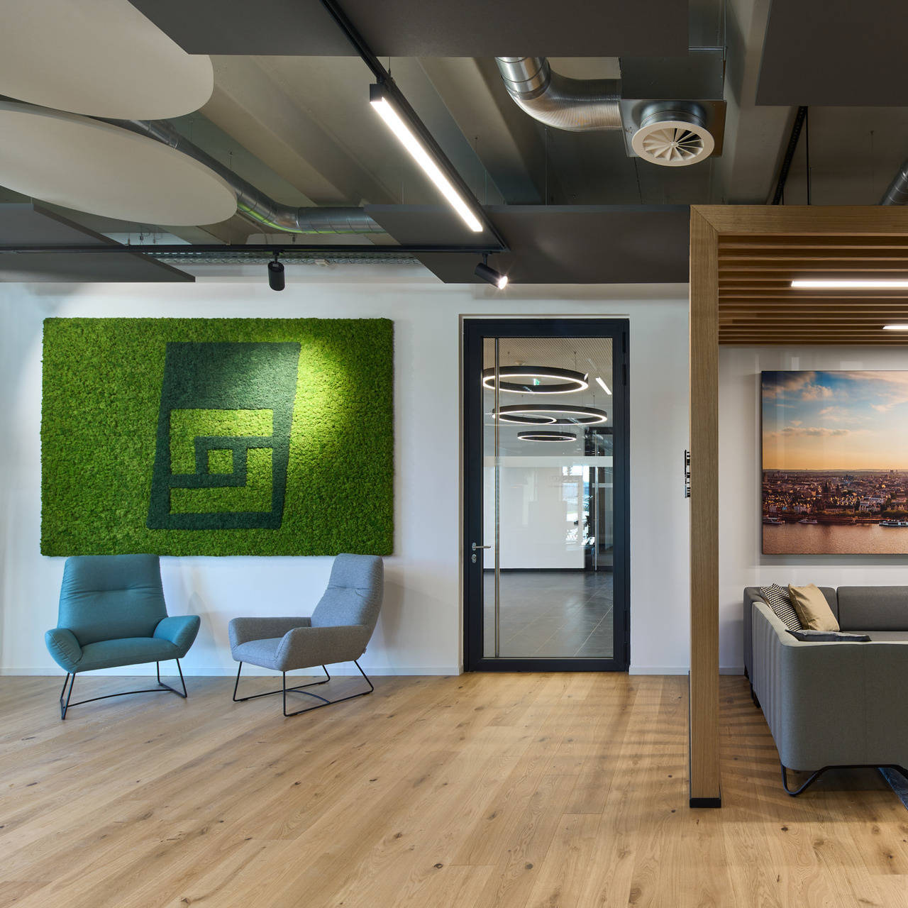 Modern office waiting area with two armchairs, green mural and large panoramic picture of Cologne above a sofa.