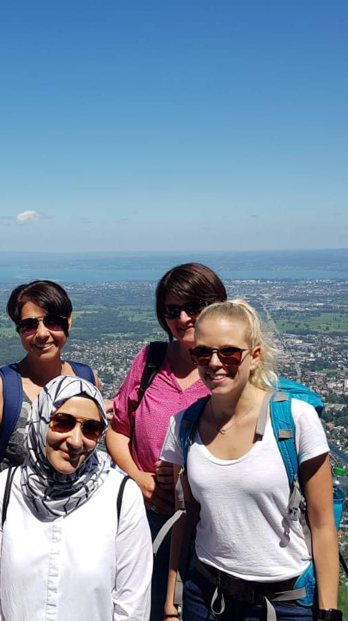 Gruppe von Frauen posiert auf einem Aussichtspunkt mit Blick über eine Stadtlandschaft bei klarem Himmel.