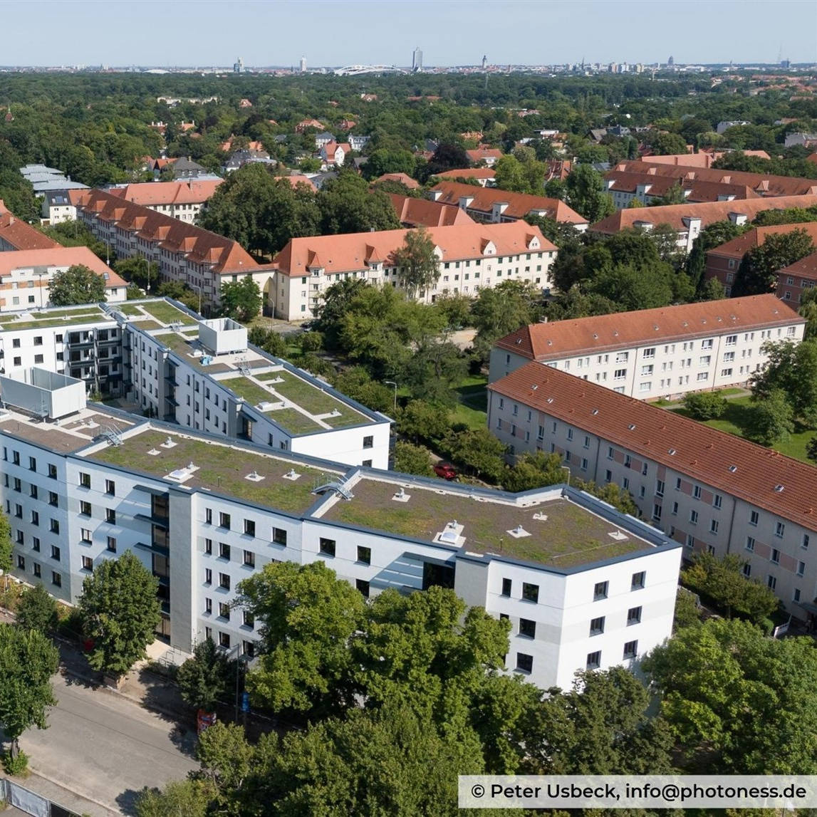 Modern residential complex with green flat roofs in a green urban environment, surrounded by trees and traditional buildings.
