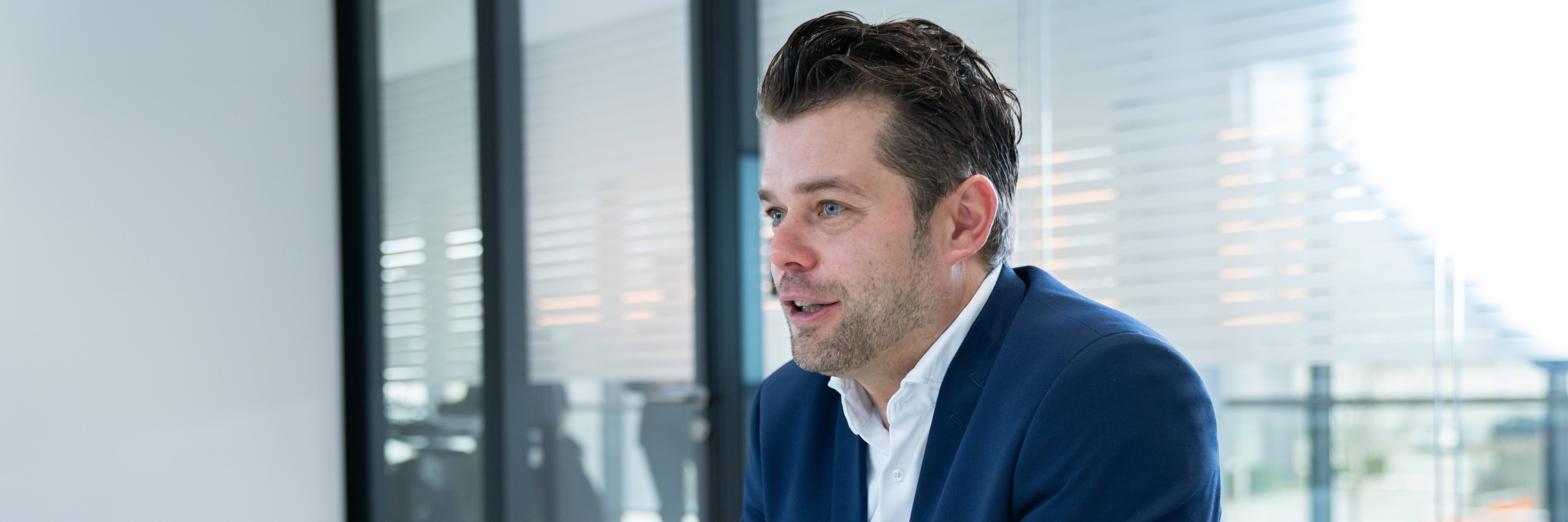 Geschäftsmann im Anzug sitzt in einem modernen Büro mit Laptop und Kaffeetasse.