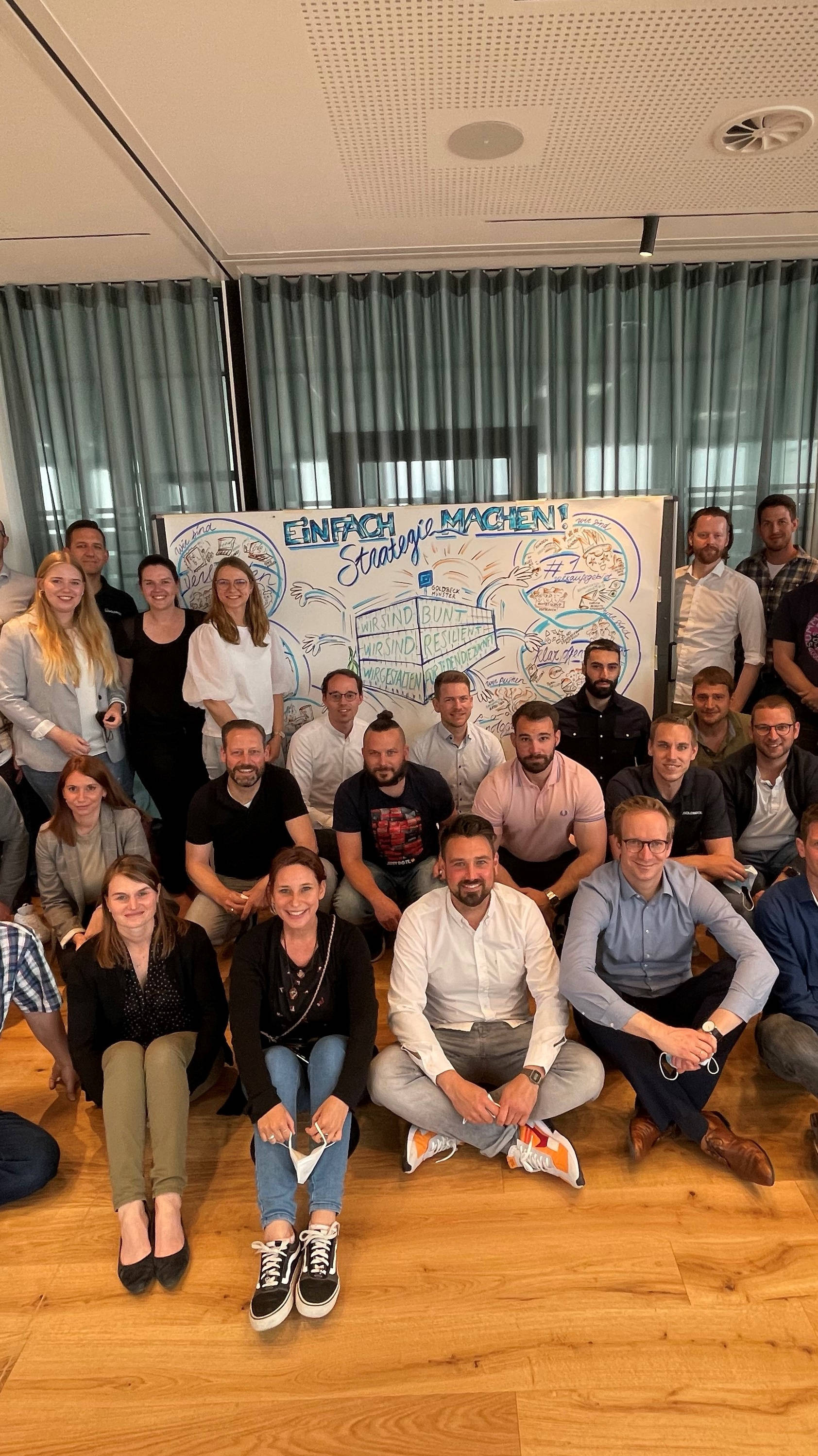 Gruppe von Menschen posiert vor einem beschrifteten Whiteboard mit der Überschrift "Einfach Strategie machen", Versammlung in einem Konferenzraum.
