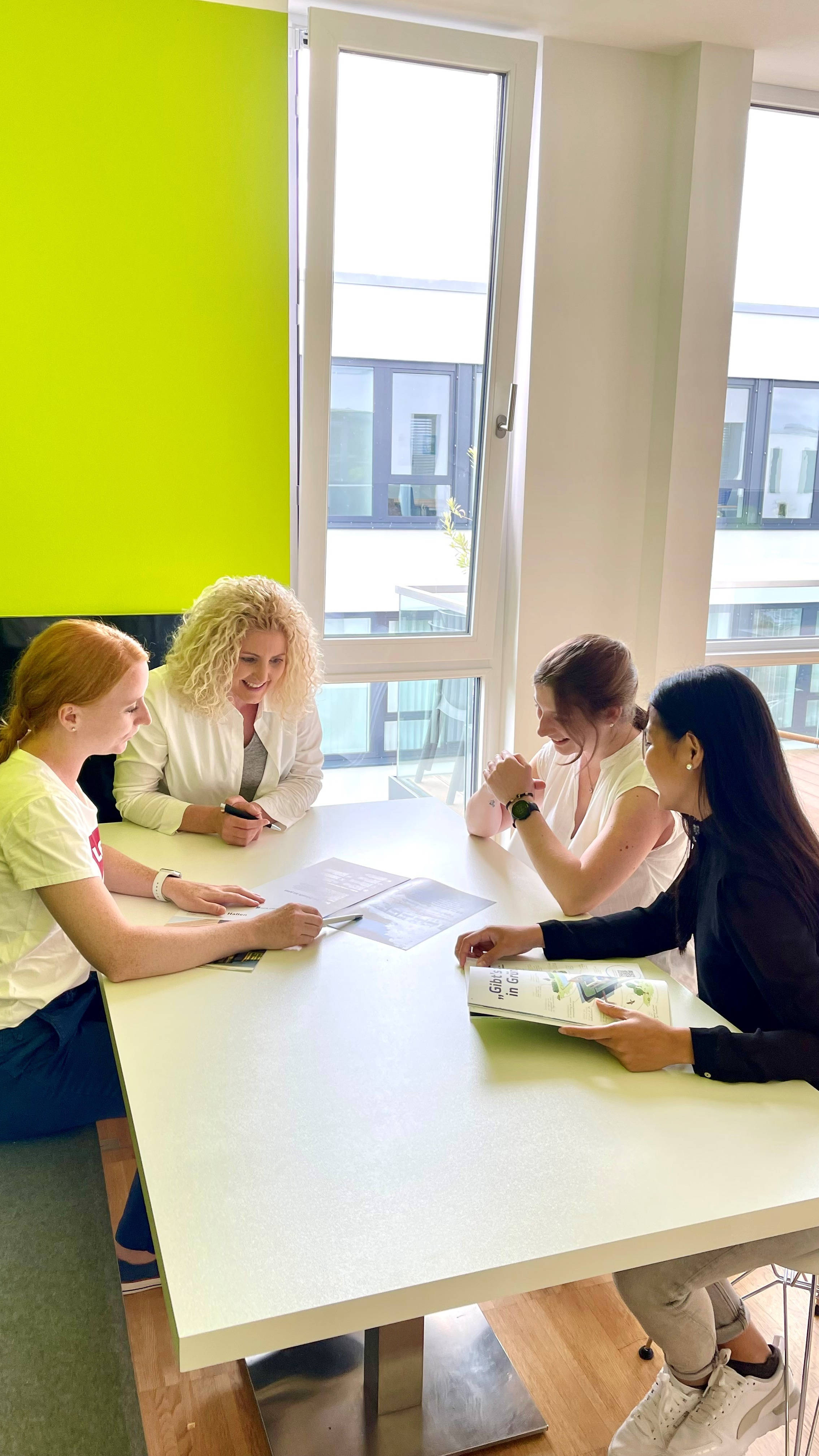 Vier Personen sitzen an einem weißen Tisch in einem modernen Büro und besprechen Dokumente.