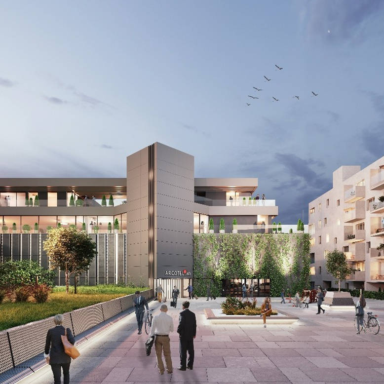 Modern architectural complex at dusk with a green inner courtyard and people walking through a lively public square.