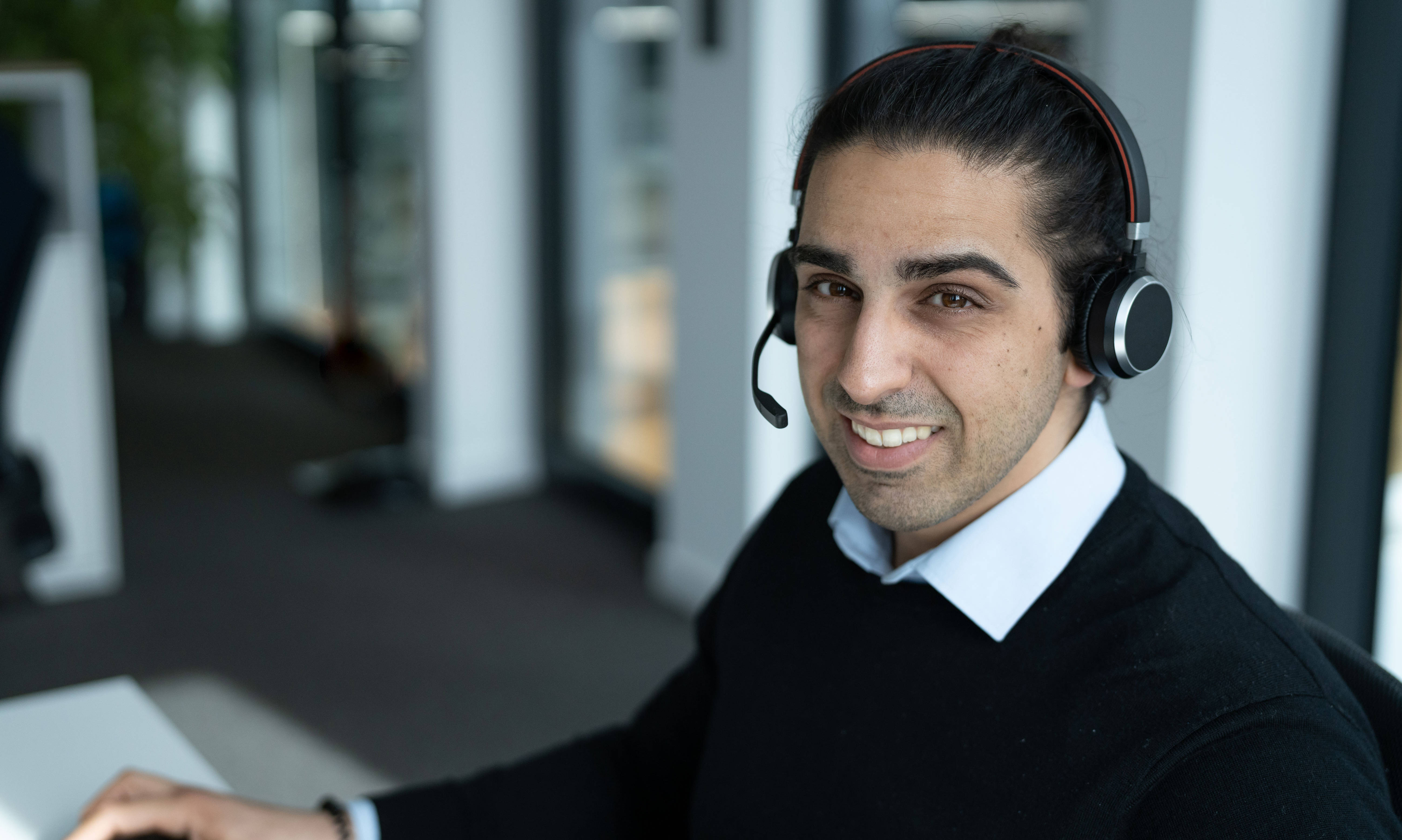 Ein Mitarbeiter mit Headset lächelt in einem modernen Büro.