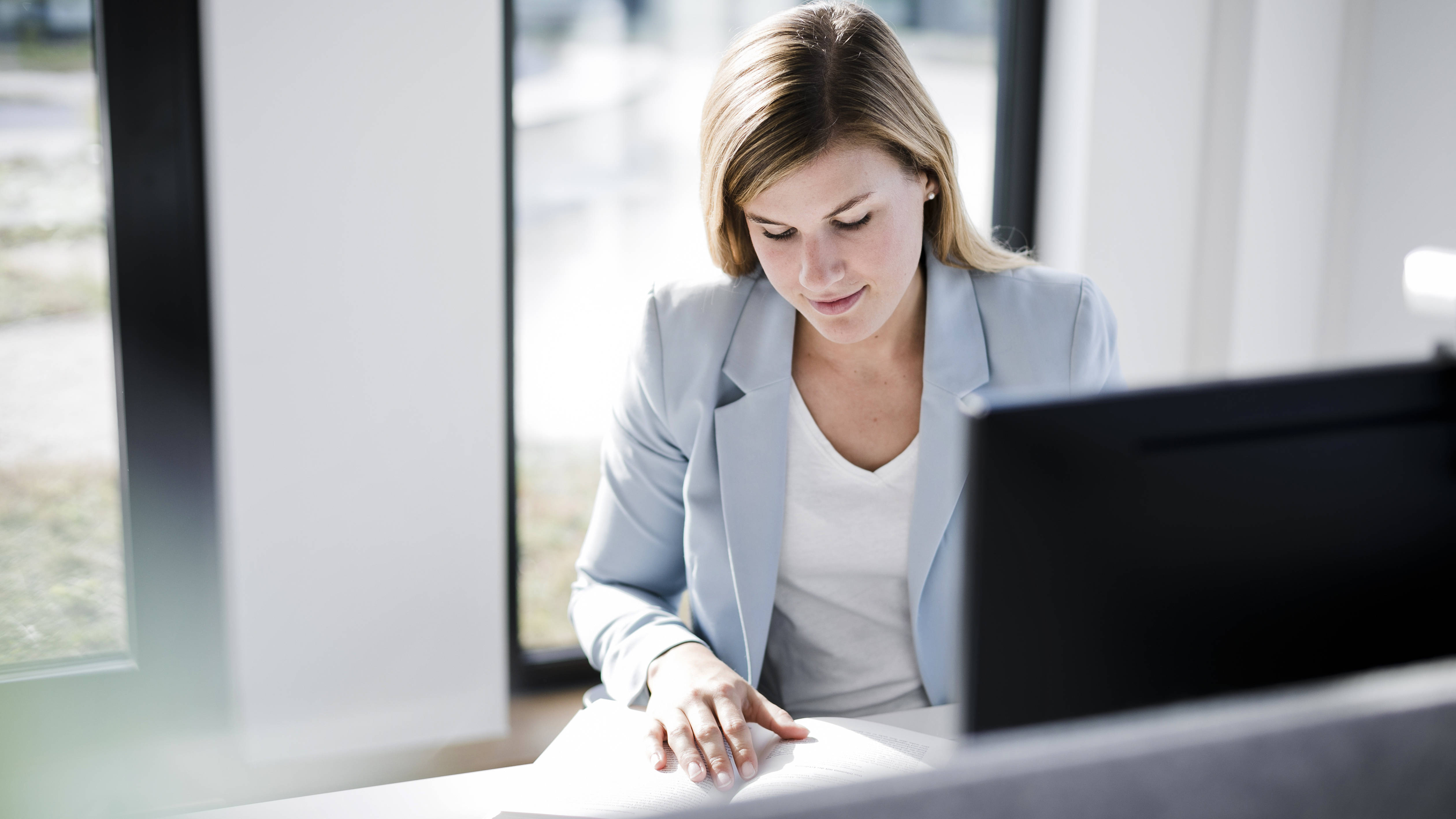 a blonde long-haired woman sits in the office and looks at documents