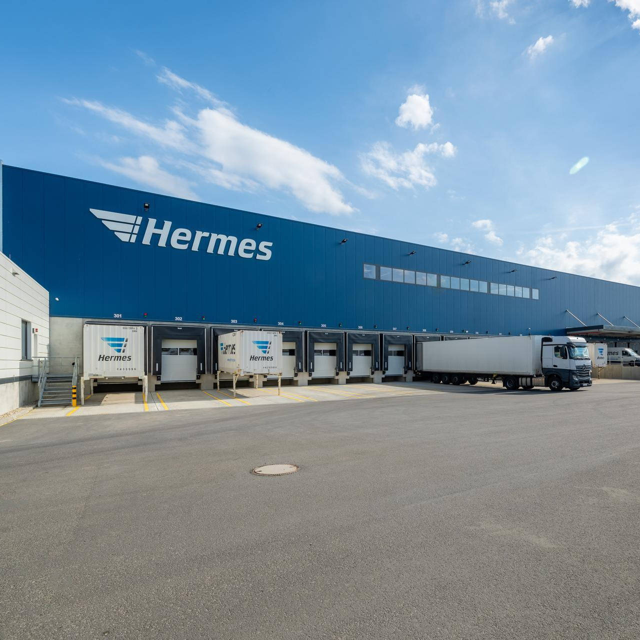 Logistikzentrum mit Hermes-Lkw an Laderampen unter blauem Himmel.