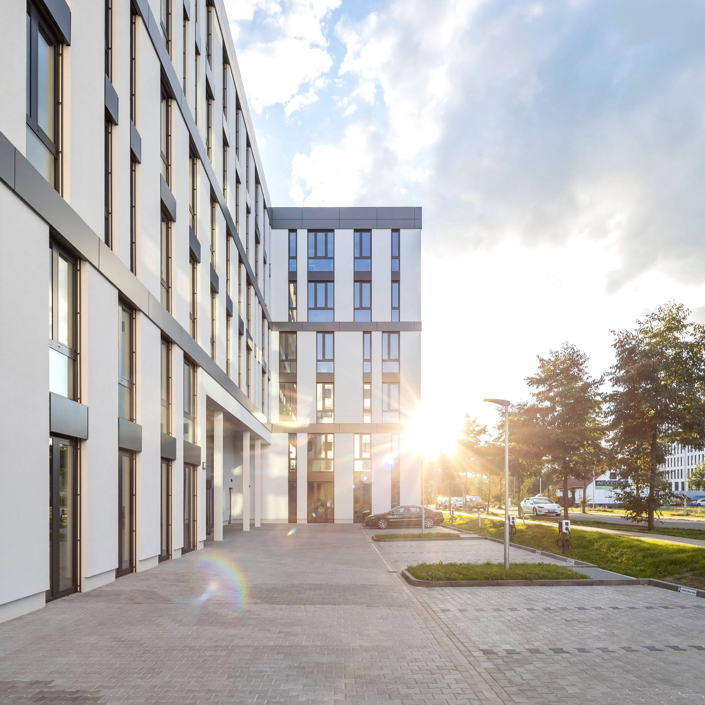 Modern office building facade at sunset, with sidewalk and trees in the foreground.