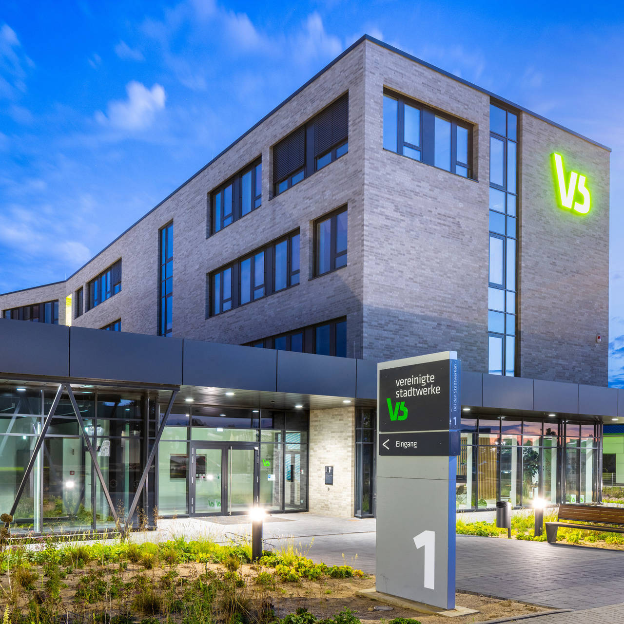 Modernes Bürogebäude der Stadtwerke Ratzeburg bei Dämmerung, mit beleuchtetem Eingang und Glasfassade.