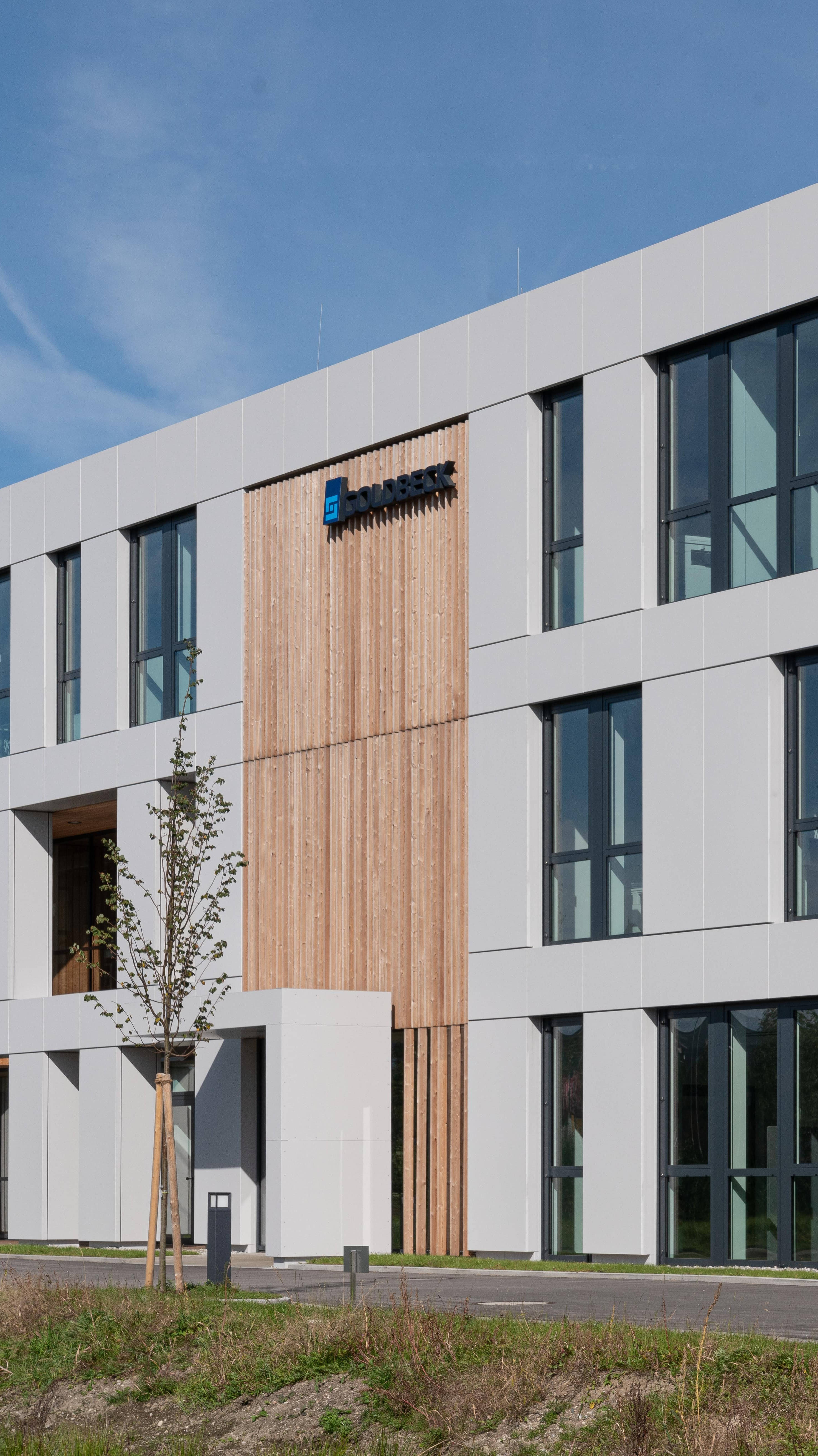 Modernes Bürogebäude mit großen Fenstern und minimalistischer Fassade, umgeben von einer Grünfläche.