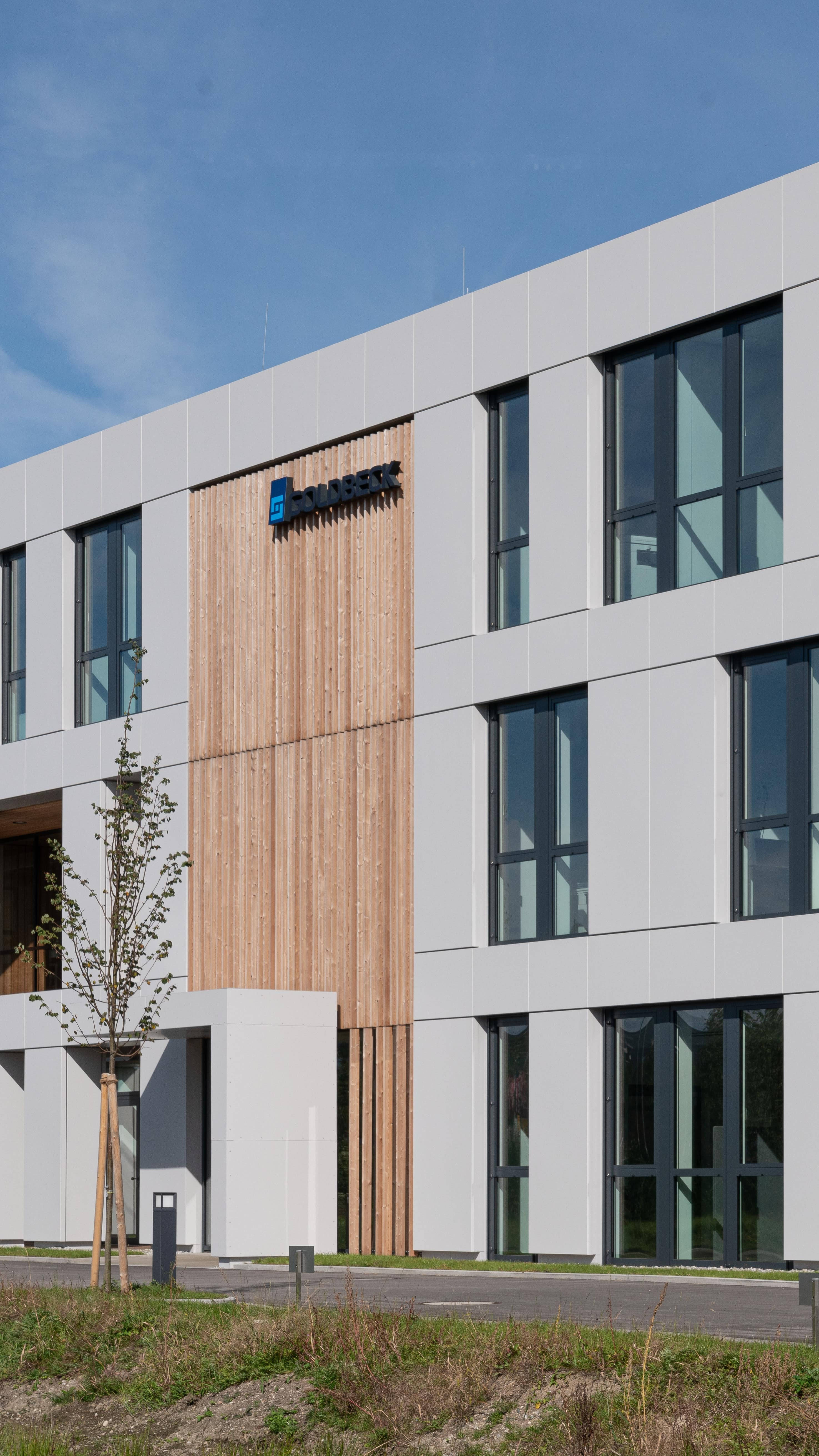 Modernes Bürogebäude mit großen Fenstern und minimalistischer Fassade, umgeben von einer Grünfläche.
