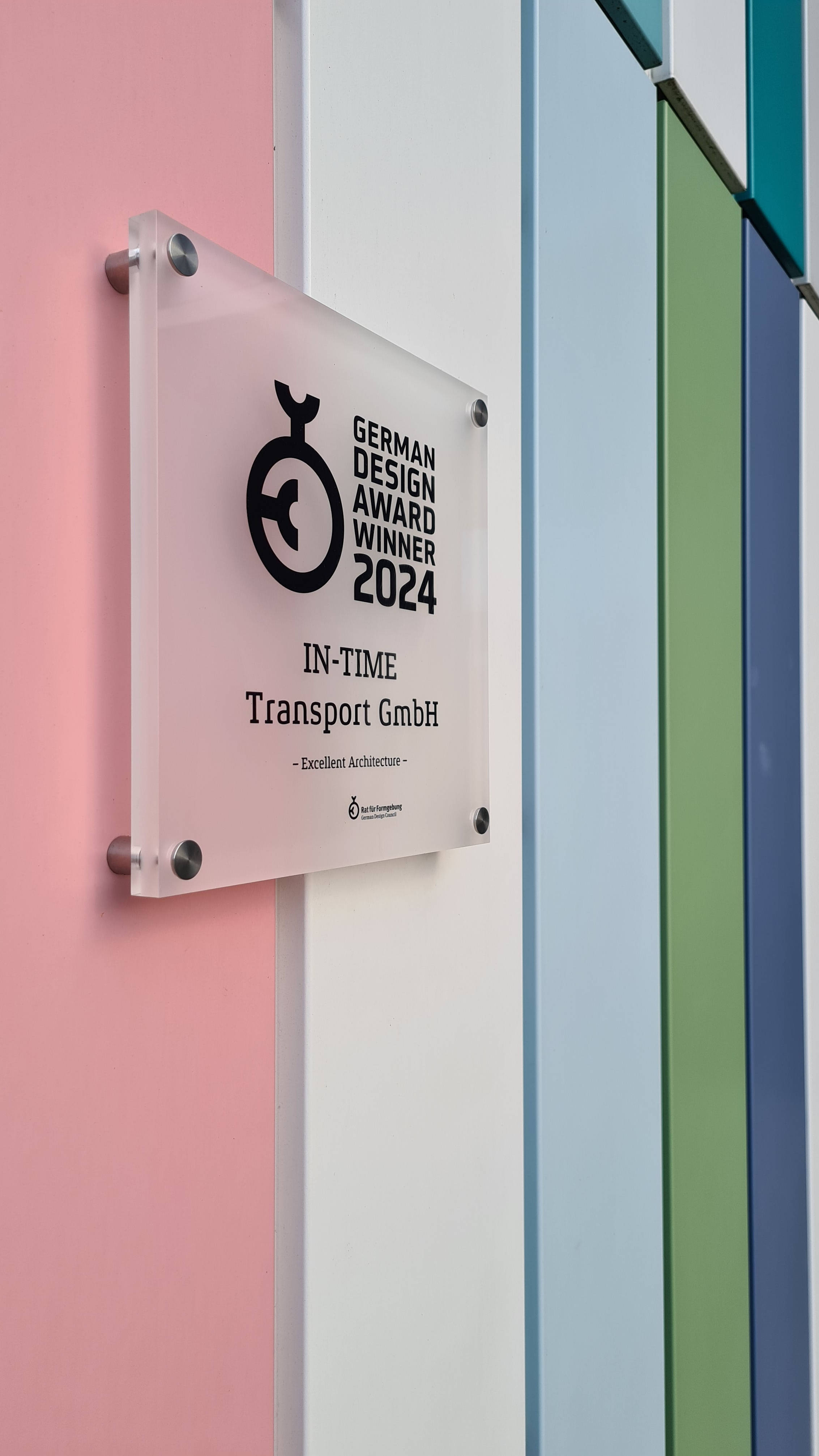 Auszeichnung "German Design Award Winner 2024" an bunter Wand montiert, prämiert IN-TIME Transport GmbH für exzellente Architektur.
