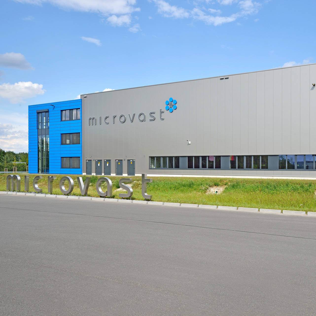Modernes graues und blaues Firmengebäude von Microvast mit einem Firmenlogo im Vordergrund, umgeben von grüner Landschaft.