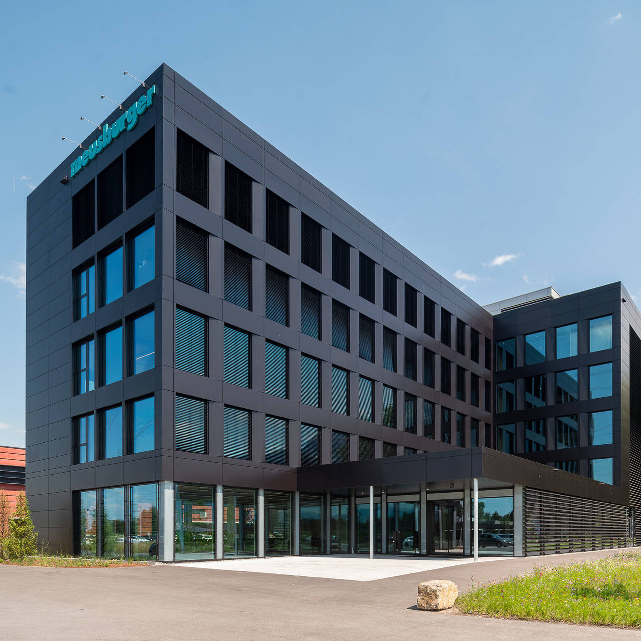 Modernes Bürogebäude mit Glasfassade unter blauem Himmel, umgeben von Grünflächen.