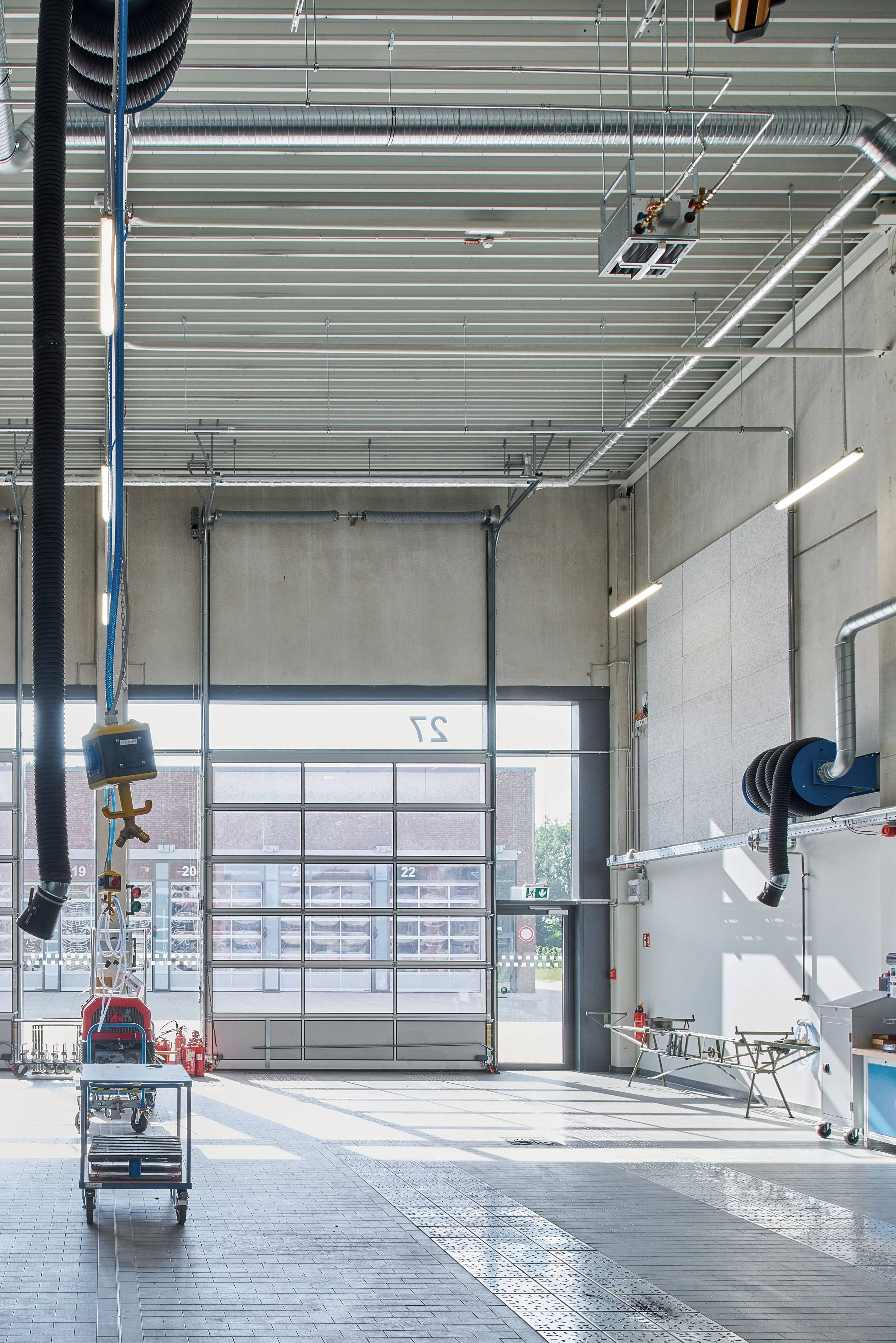 Moderne Werkstatt mit hohen Decken, ausgestattet mit Lüftungsrohren, Arbeitsbereichen und großen Garagentoren.