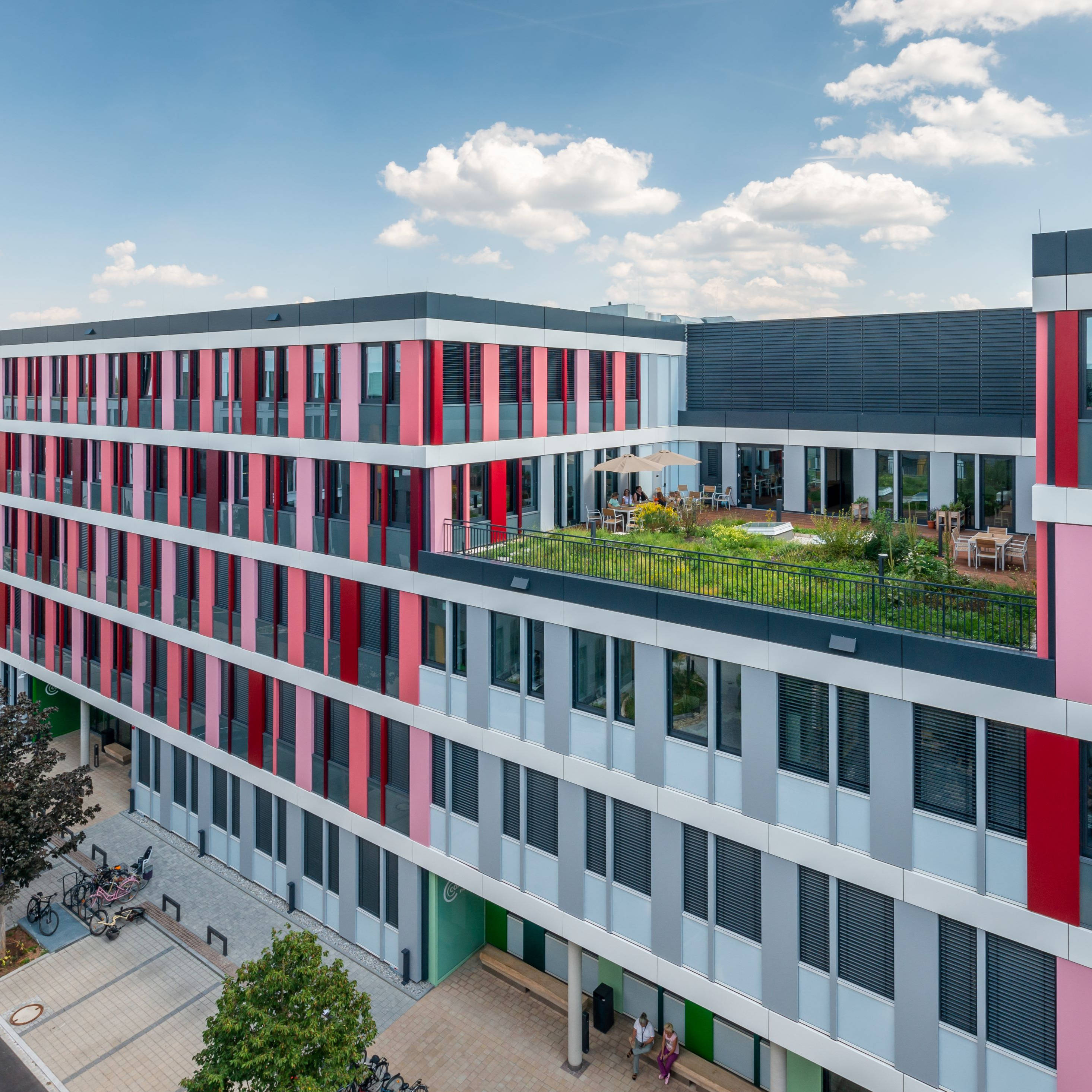 Modern office building with colorful façade and green courtyard in an urban environment, in sunny weather.