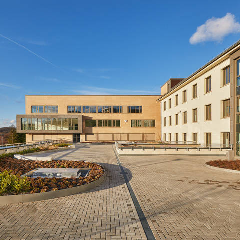 Modernes Bürogebäude mit Glasfassade und bepflanztem Vorplatz bei klarem Himmel.
