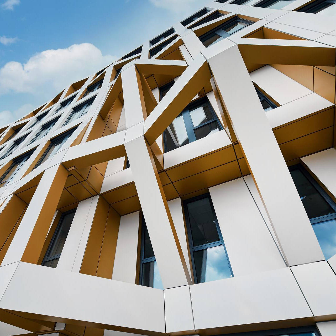 Modernes Gebäude mit geometrischer Fassade und großen Fenstern vor blauem Himmel.