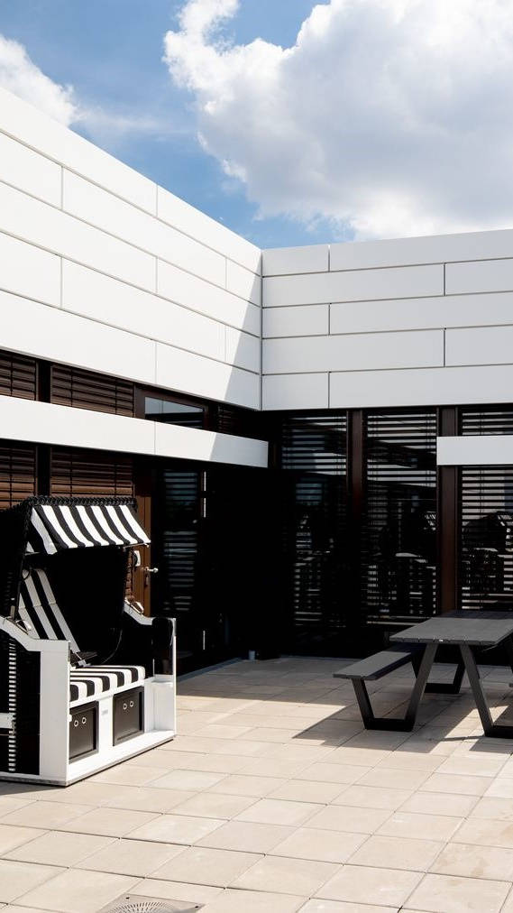 Modern inner courtyard with beach chair and wooden seating set, framed by white building walls under a blue sky.