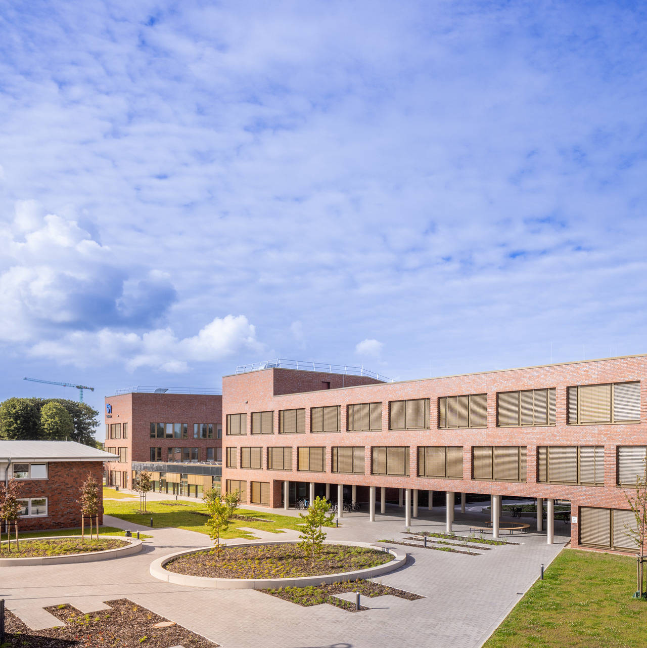 Moderne Backsteinfassade eines Schulgebäudes mit grüner Umgebung und bewölktem Himmel.
