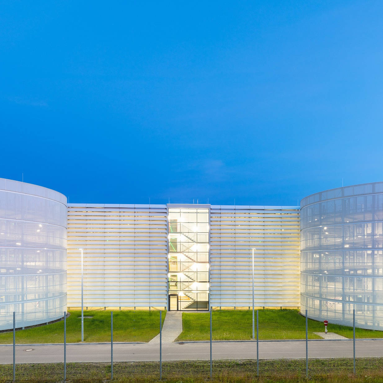 Modernes Gebäude mit runden, beleuchteten Fassaden und Glasfront, aufgenommen bei Dämmerung.