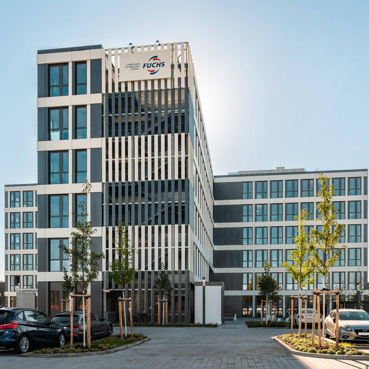 An office building with many windows surrounded by a large car park for vehicles.