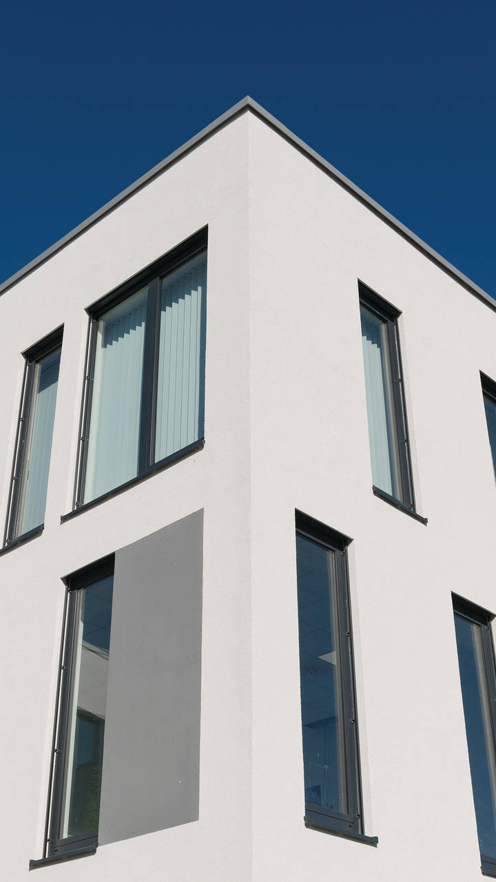 Moderner Bürogebäudekomplex mit weißen Fassaden, großen Fenstern und Bäumen im Vordergrund bei blauem Himmel.