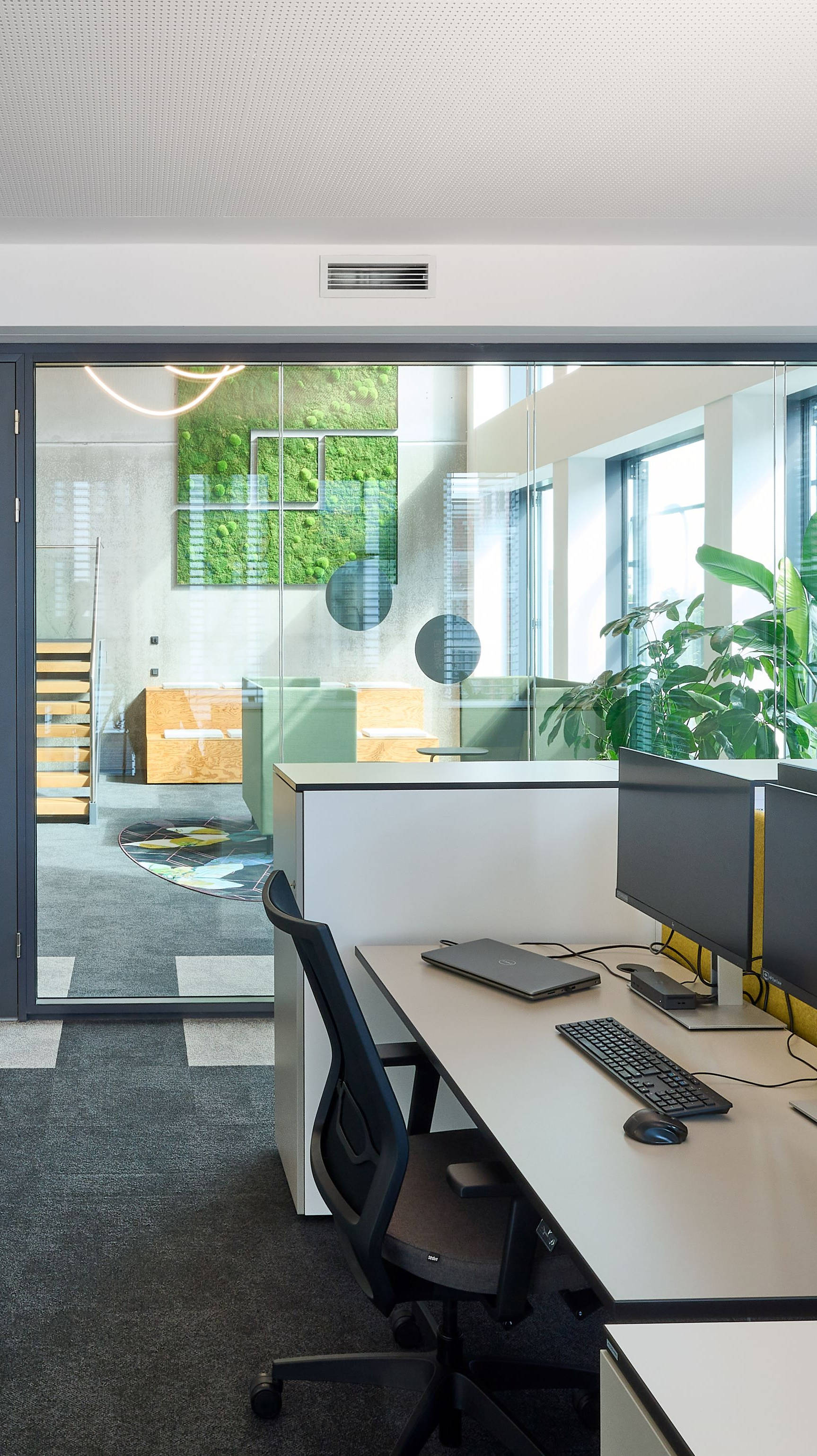 Modernes Büro mit vertikalem Indoor-Garten und Computerarbeitsplätzen neben großen Fenstern.
