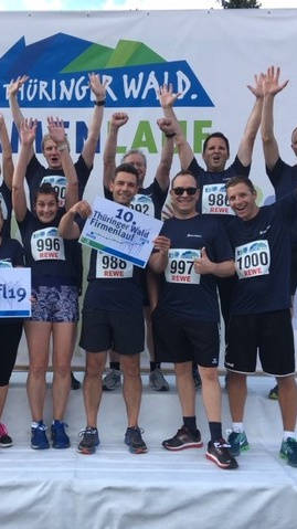 Läufergruppe jubelt nach dem Thüringer Wald Firmenlauf, trägt Startnummern und hält Schilder hoch.