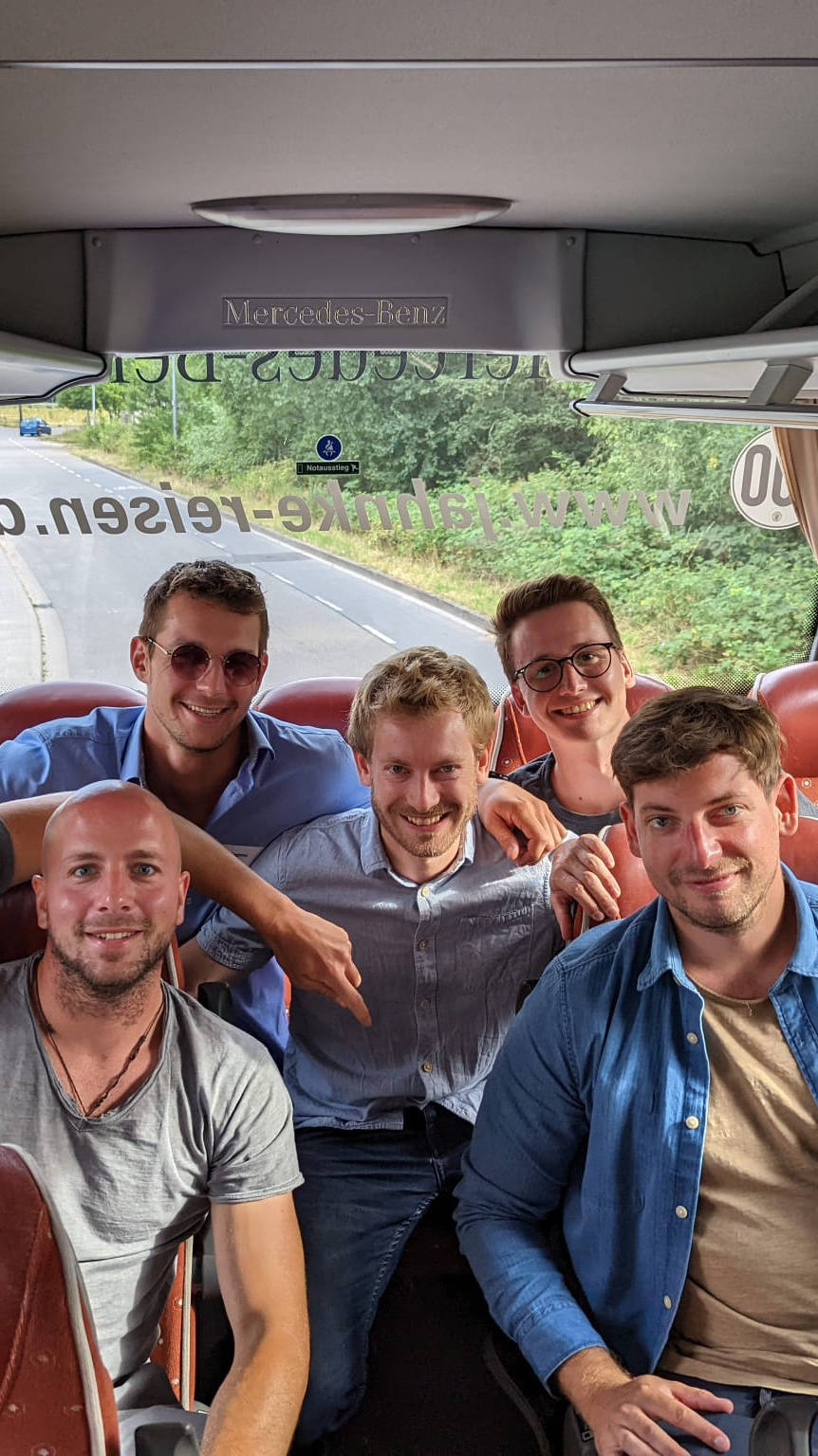 Gruppe von sieben Personen in einem Bus auf roten Sitzen lächelnd in die Kamera.
