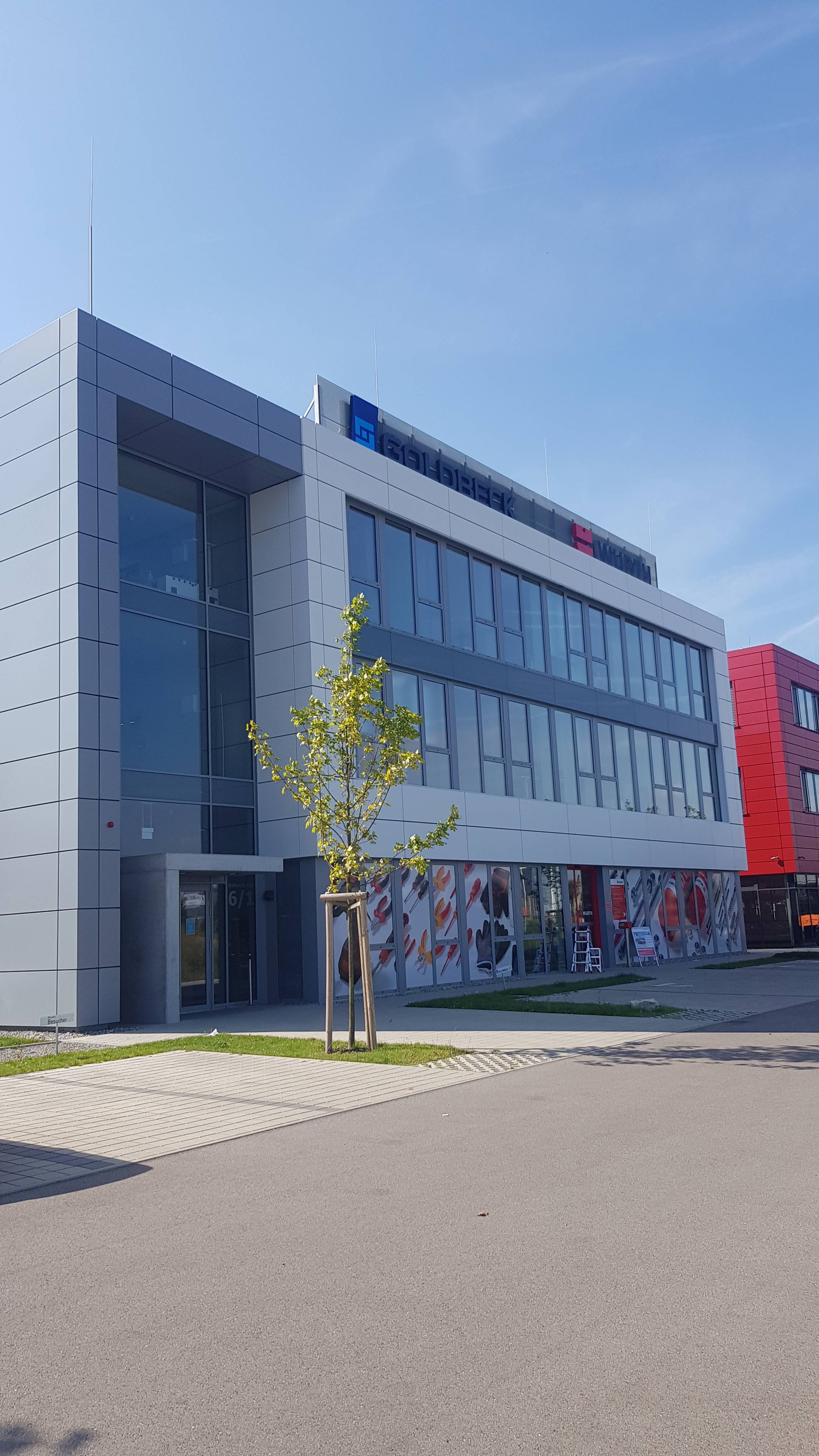 Modernes Bürogebäude mit Glasfassade und Werbebannern, blauer Himmel im Hintergrund.