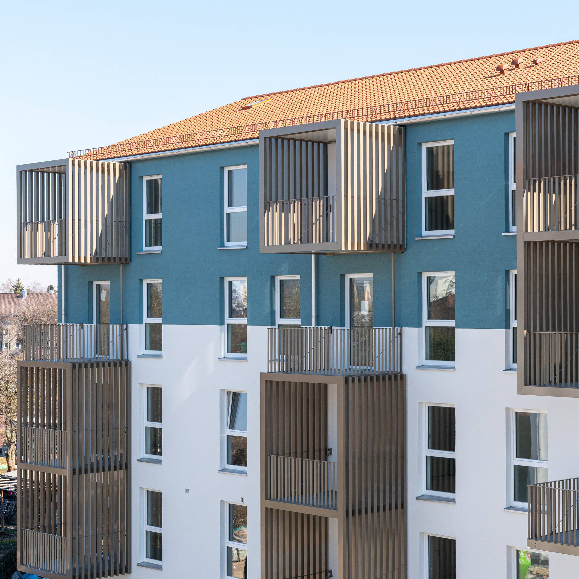 Modern apartment building with blue and white façade and large balconies, under a blue sky.