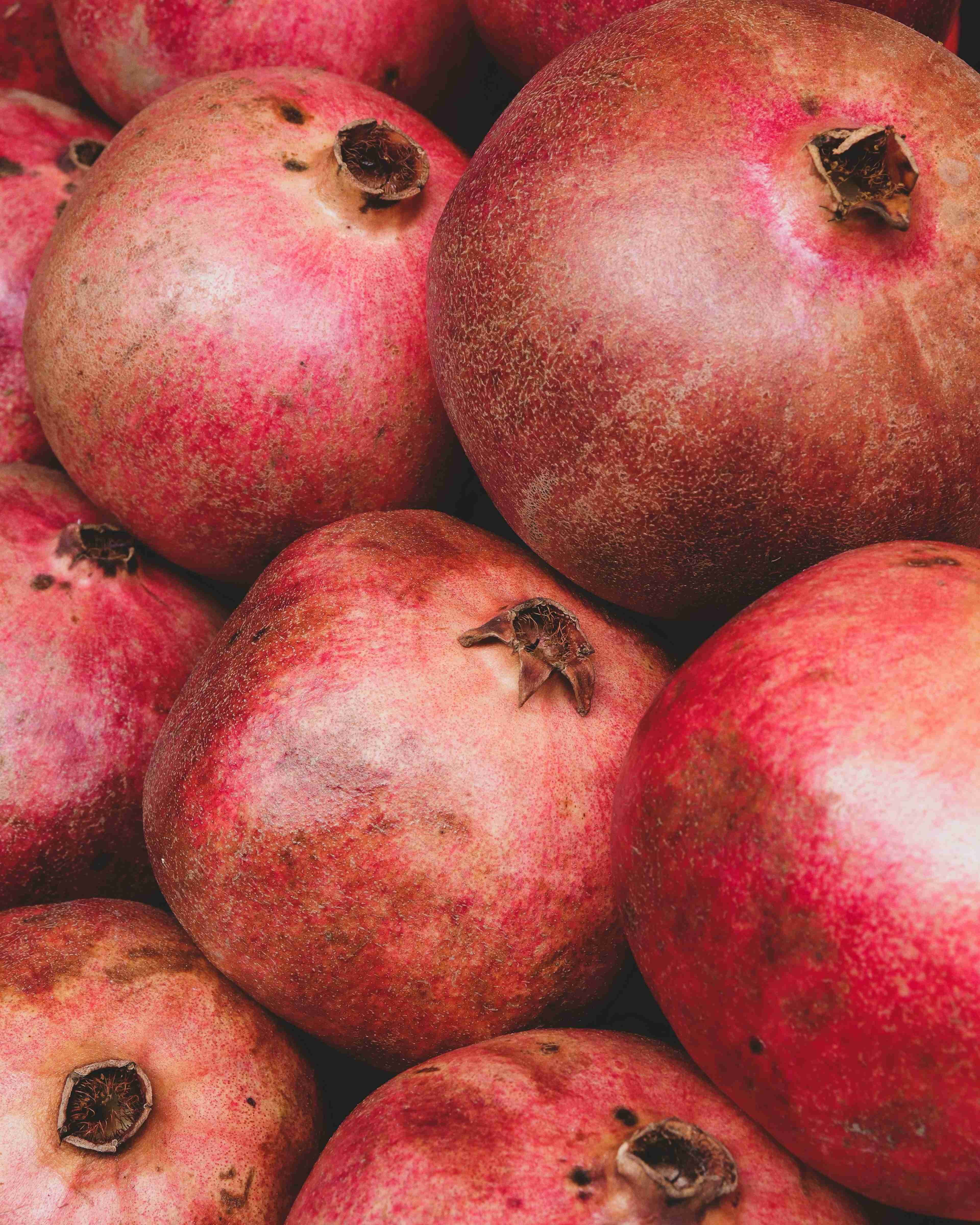 Close-up of a group of pomegranates with rich red and pinkish hues, showcasing their natural mottled textures and crown-like stems.