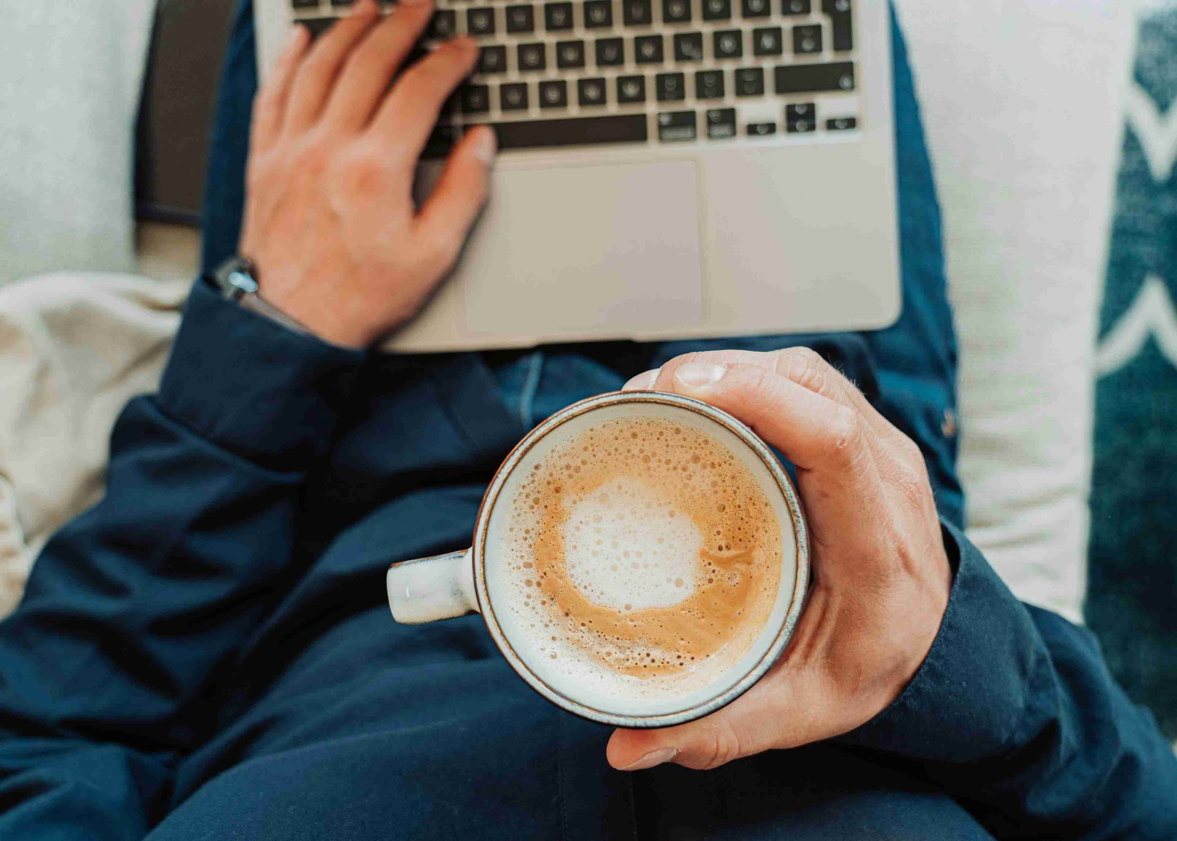 Man holding white ceramic mug with coffee in it whilst working on a MacBook Air